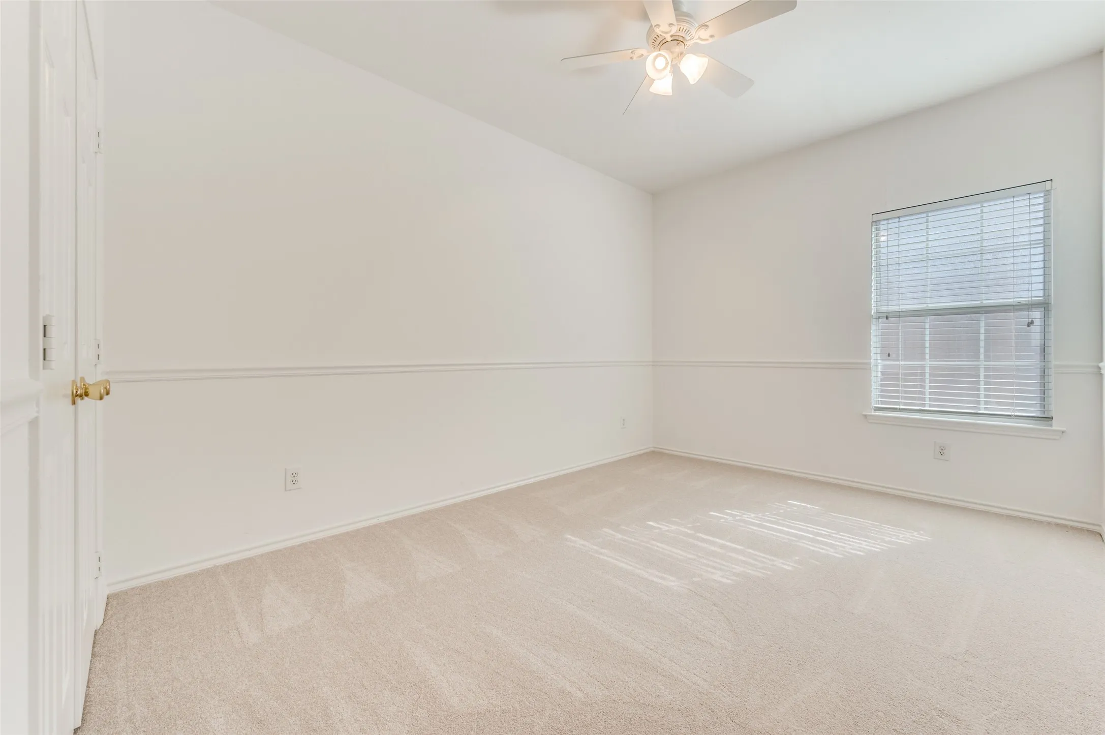 This is one of the two bedrooms located on the east side of the home.  Vaulted ceiling, ceiling fan, neutral carpet flooring, single window with blinds, and white paneled doors