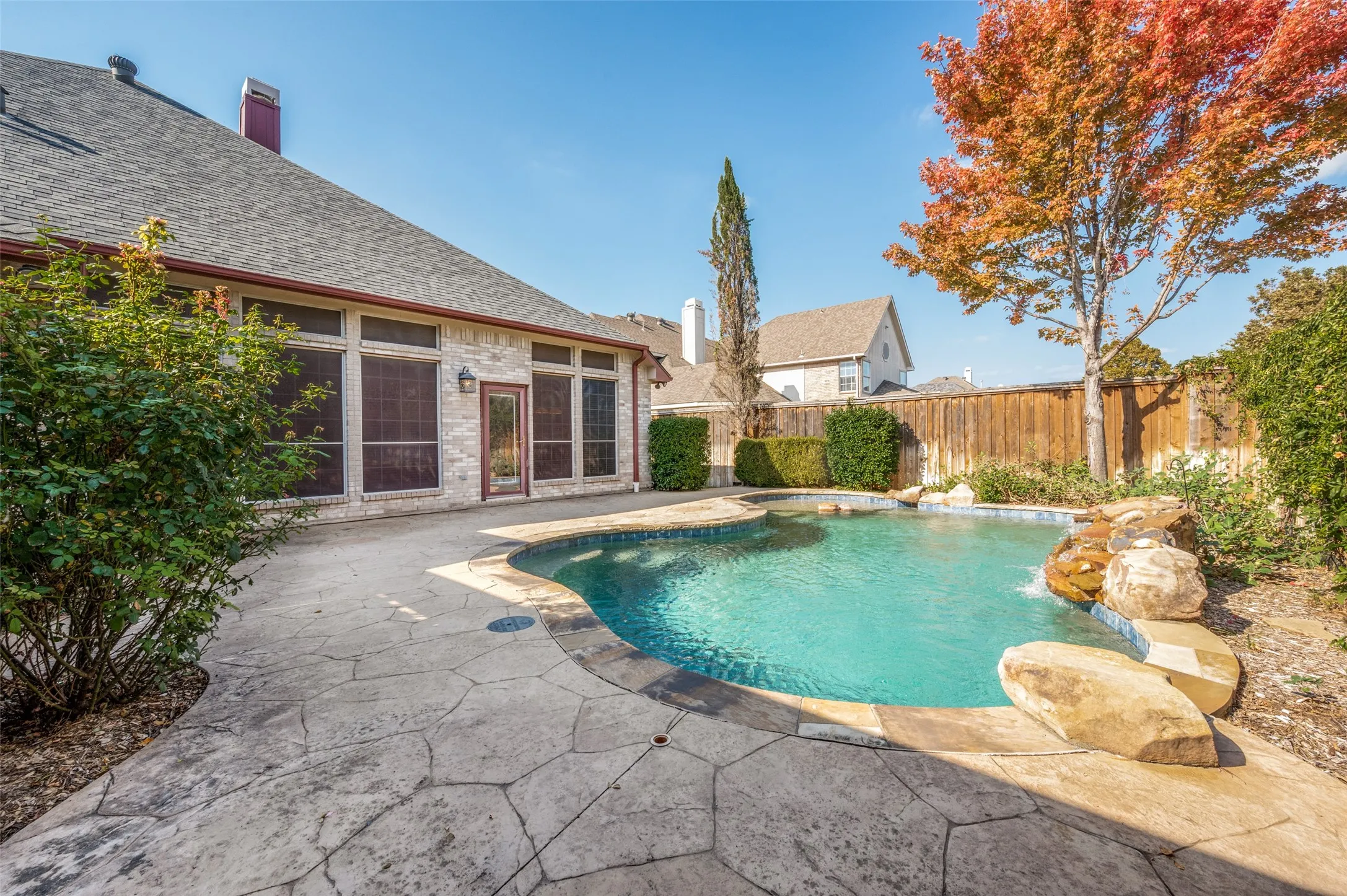 Swimming pool with a rock waterfall feature, stamped concrete patio, and privacy fencing.  The fence was recently stained, though this picture doesn't show it.