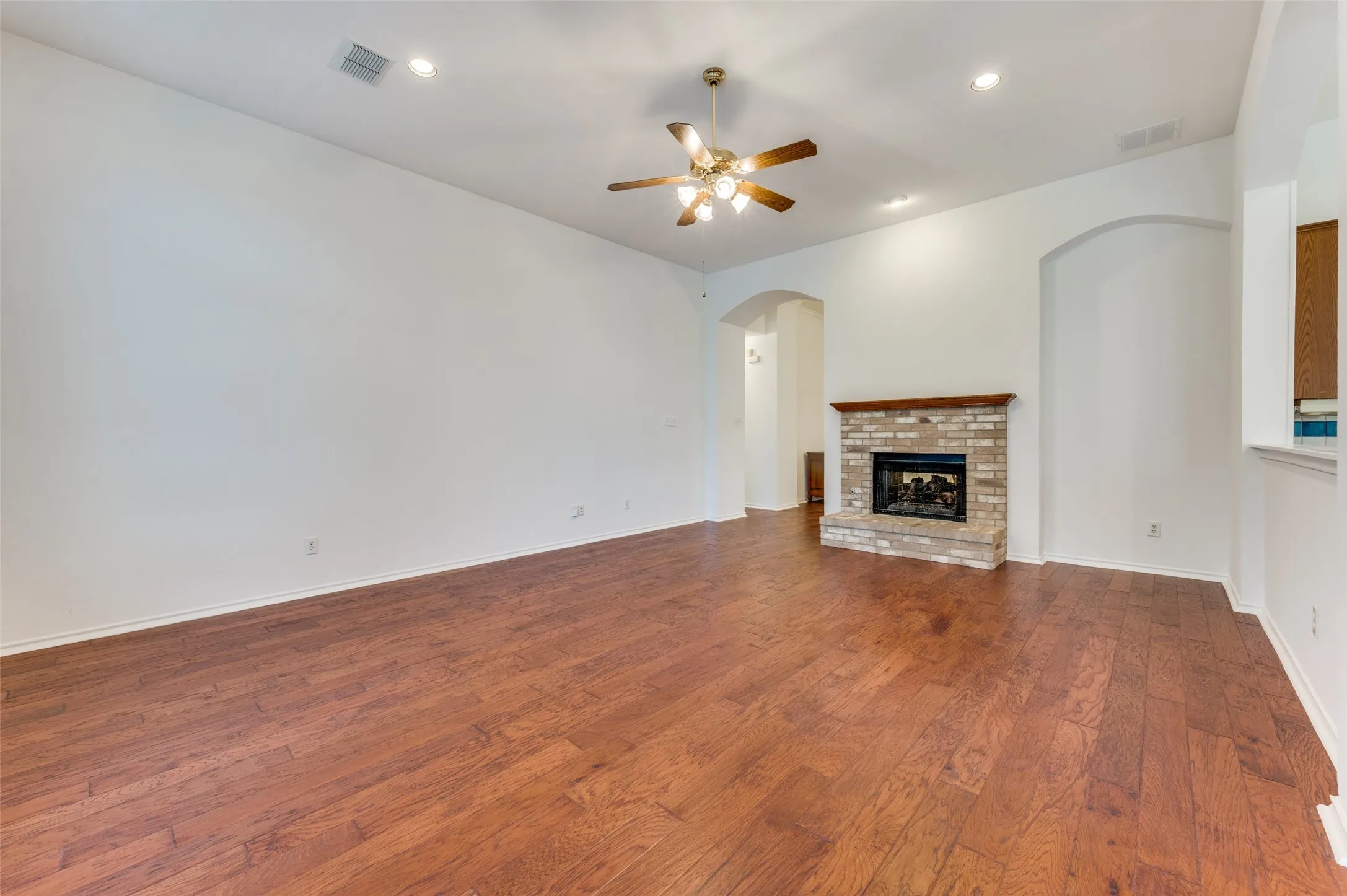 Wood-finish flooring, recessed lighting, ceiling fan, brick fireplace with wood mantel, and arched doorways