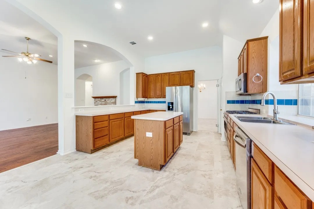 Kitchen featuring a central island, wood cabinetry, stainless steel appliances, and a tile backsplash.  The picture is taken from the breakfast area directly connected to the kitchen.