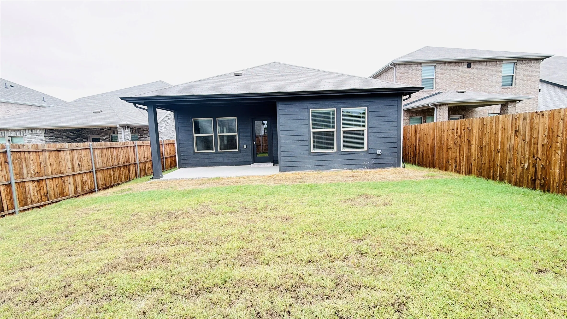 Expansive backyard featuring a privacy fence, covered concrete patio, and dark exterior siding