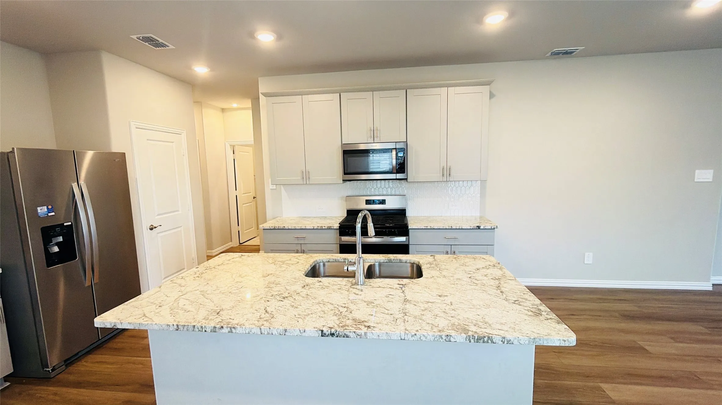 Modern kitchen featuring a large island with an undermount sink, stainless steel appliances, light-toned cabinetry, and wood-finish flooring
