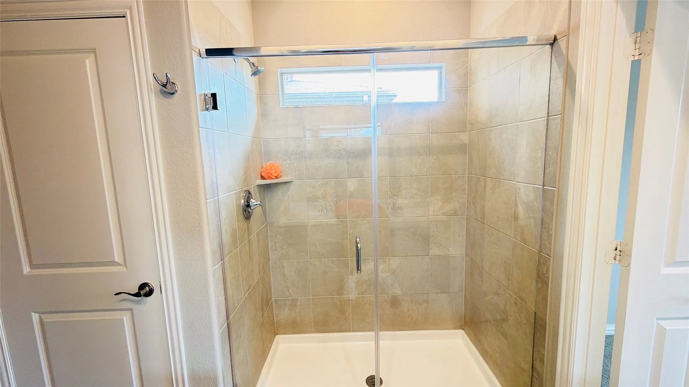 Glass-enclosed shower with tile surround, built-in shelf, and transom window