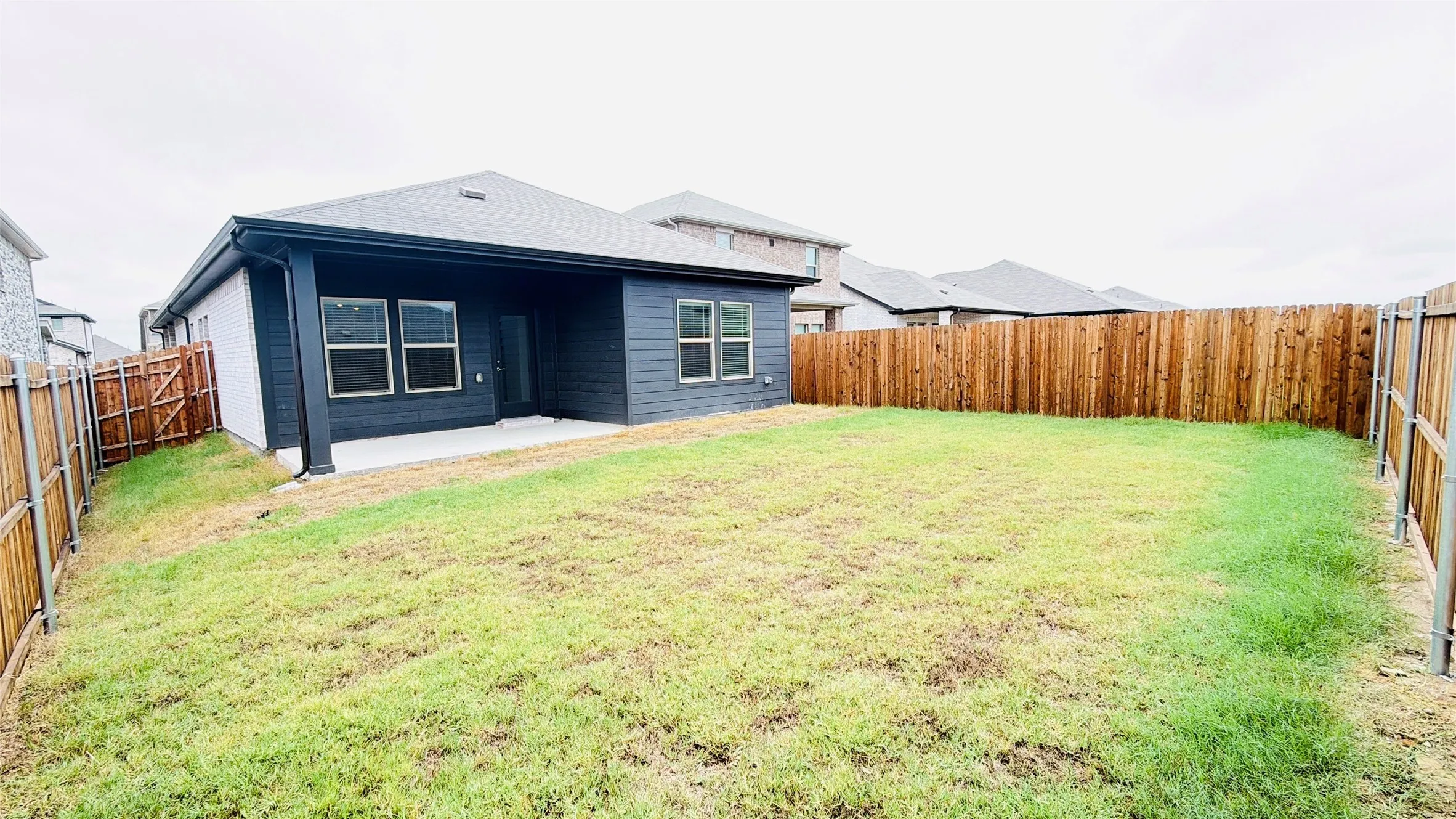 Backyard featuring a concrete patio, wood privacy fencing, and a dark-toned exterior with multiple windows