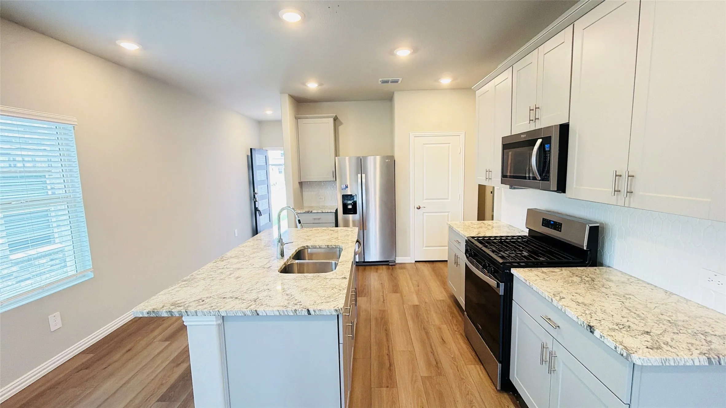 Kitchen featuring stainless steel appliances, light-toned cabinetry, a double basin sink, and granite countertops, with wood-finish flooring