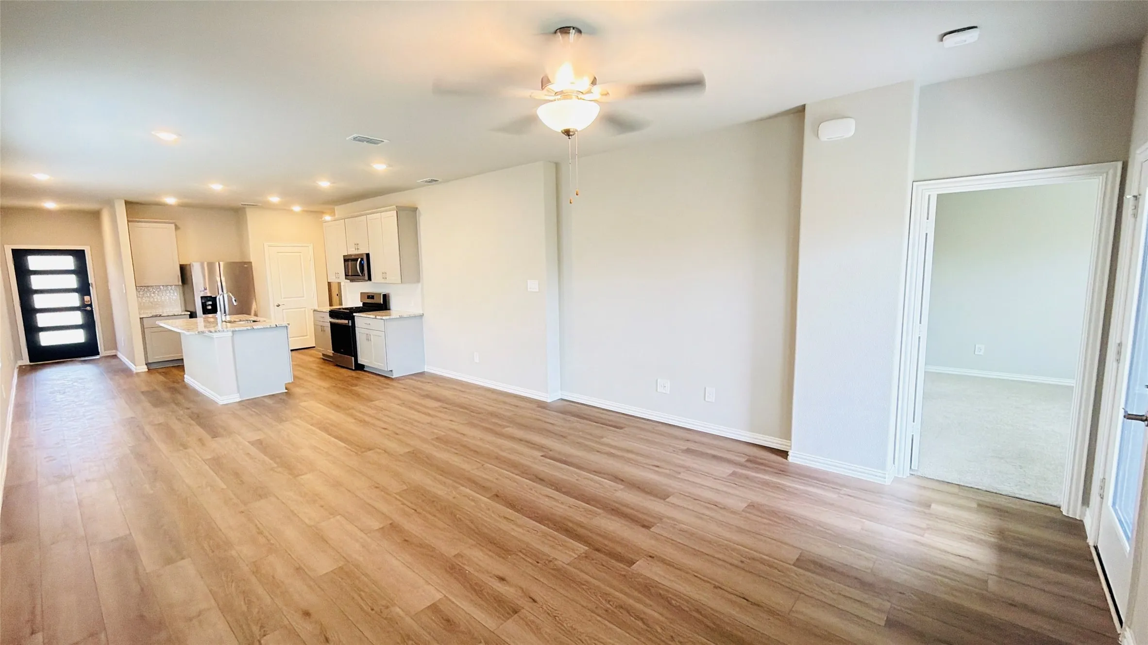 Open-concept living area with wood-finish flooring, a kitchen island, stainless steel appliances, recessed lighting, and a ceiling fan