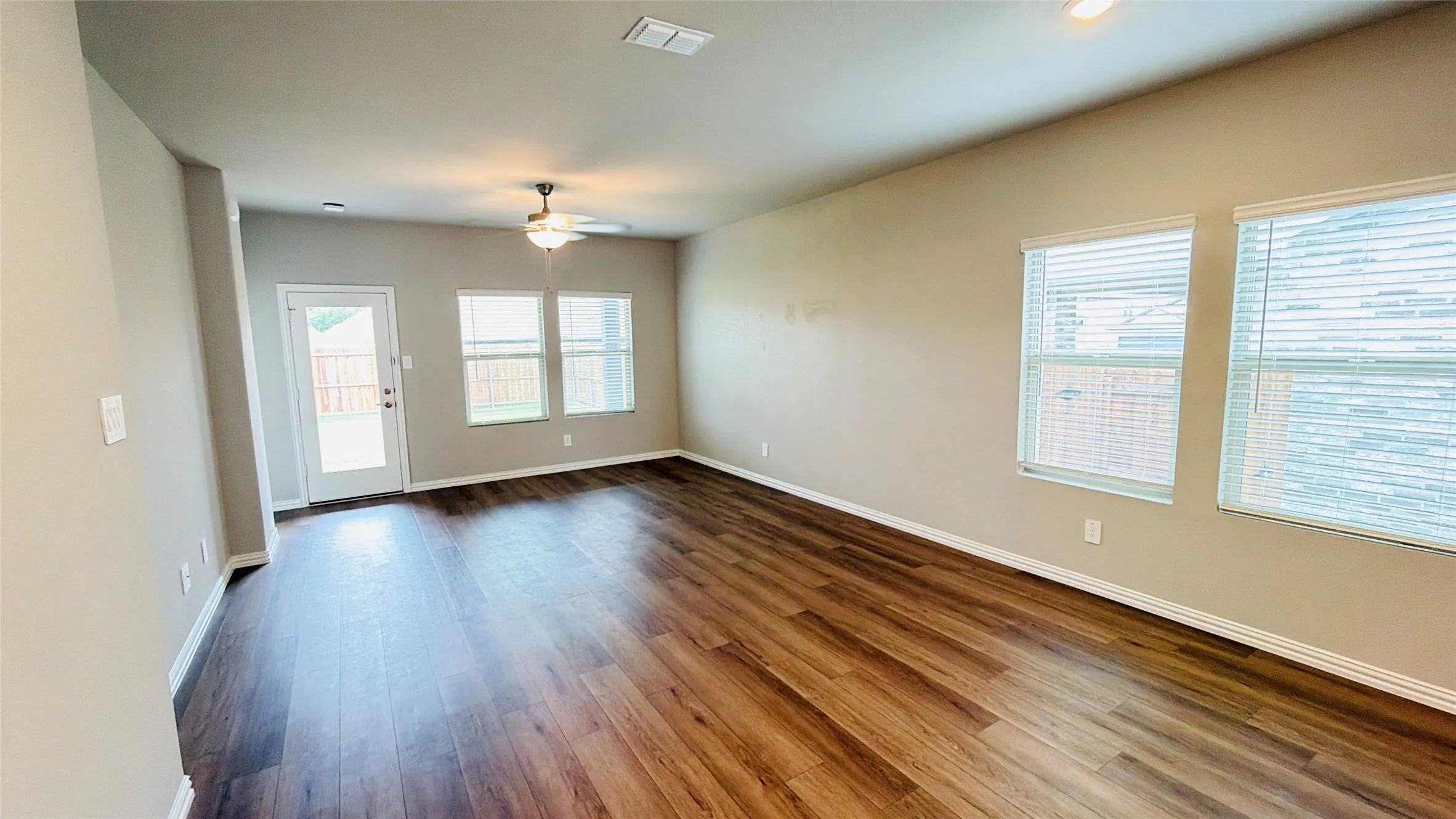 Wood-finish flooring, multiple windows with blinds, recessed lighting, ceiling fan, and a rear door providing exterior access