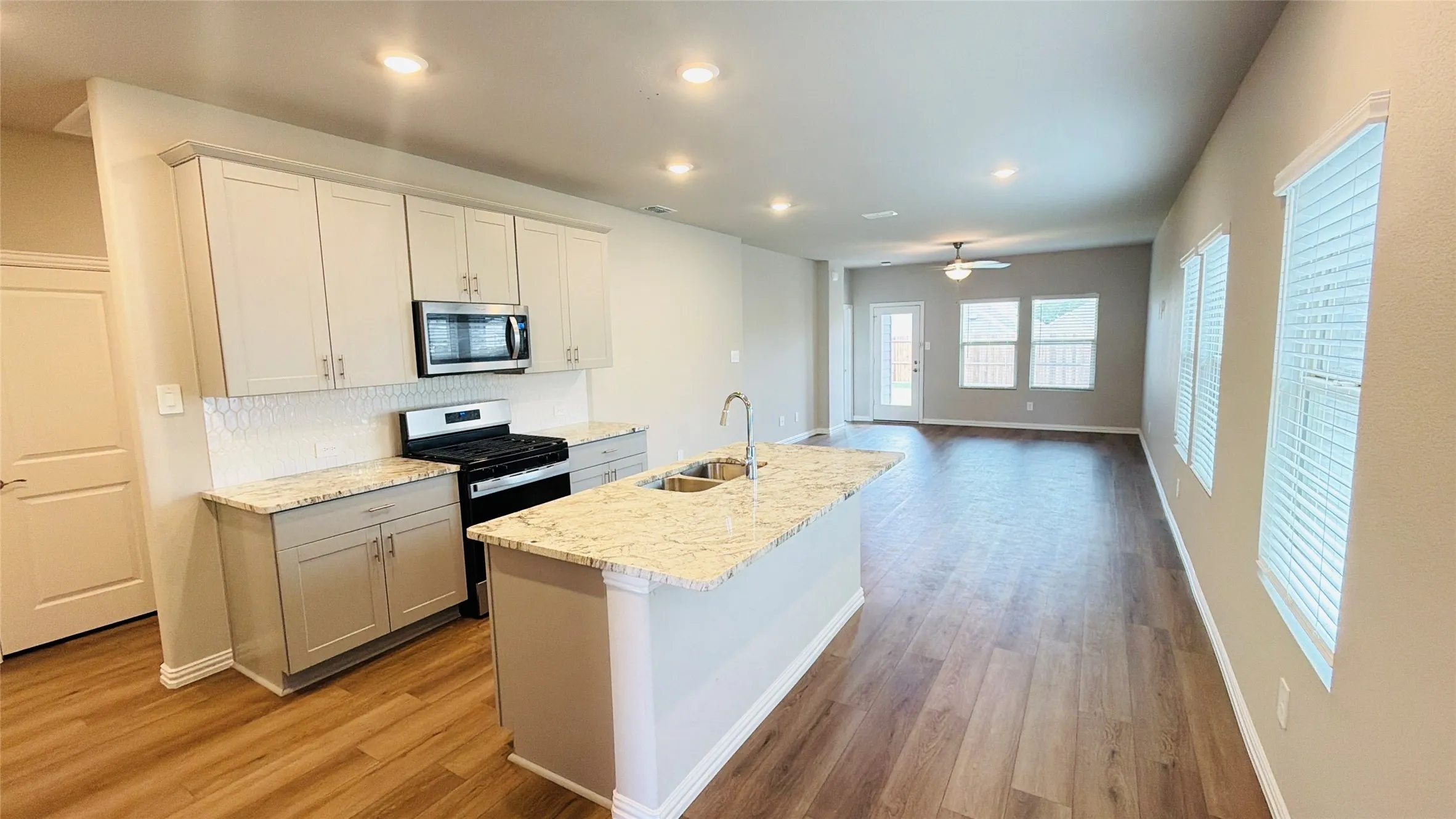 Kitchen island with double basin sink, light-toned cabinetry, stainless steel microwave, gas range, and wood-finish flooring throughout