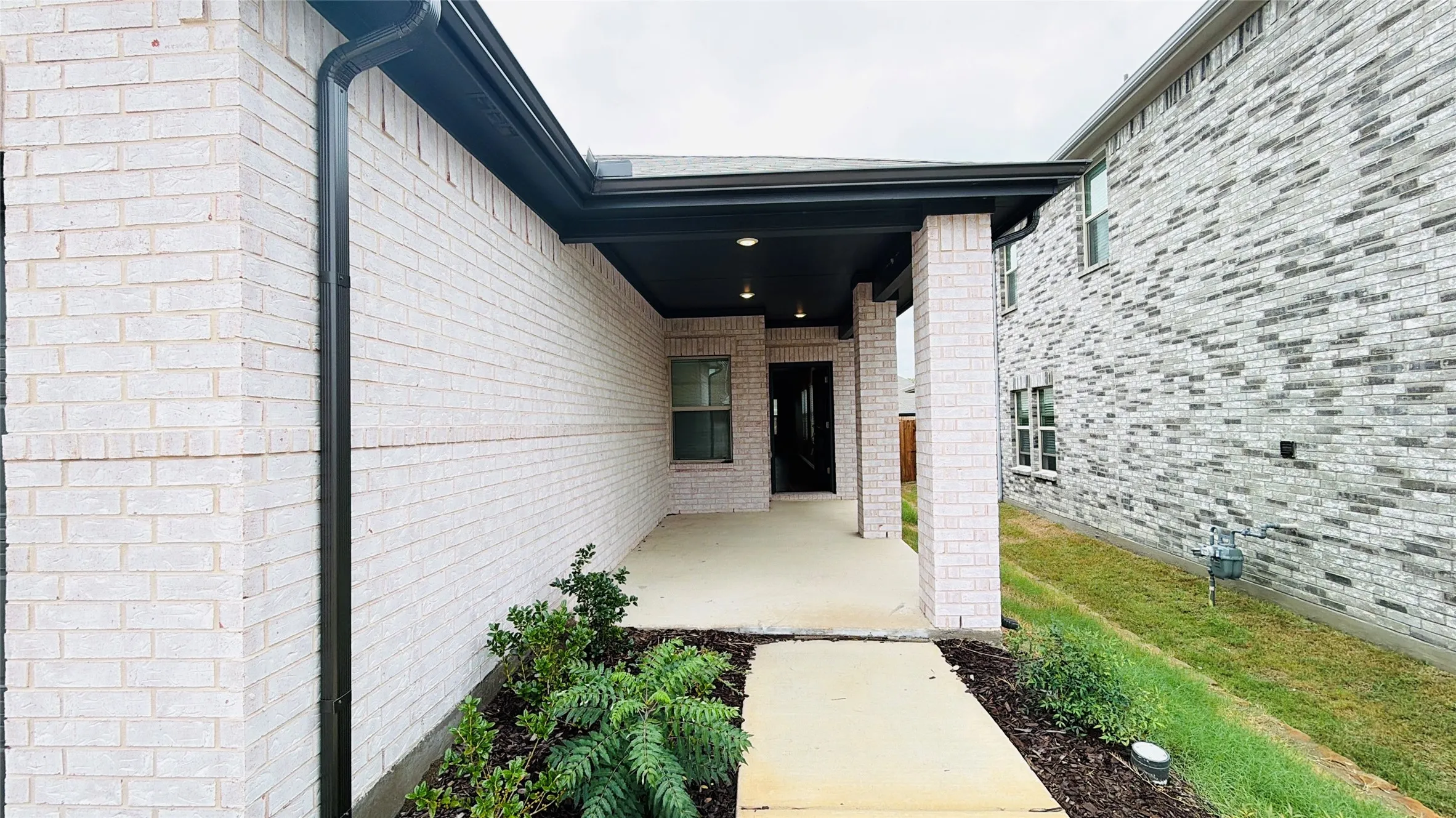 Covered entry with recessed lighting, brick columns, and a concrete walkway