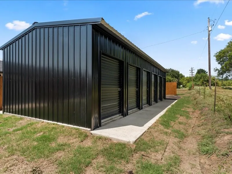 STORAGE available on property. Black corrugated metal siding with multiple roll-up doors and a concrete walkway