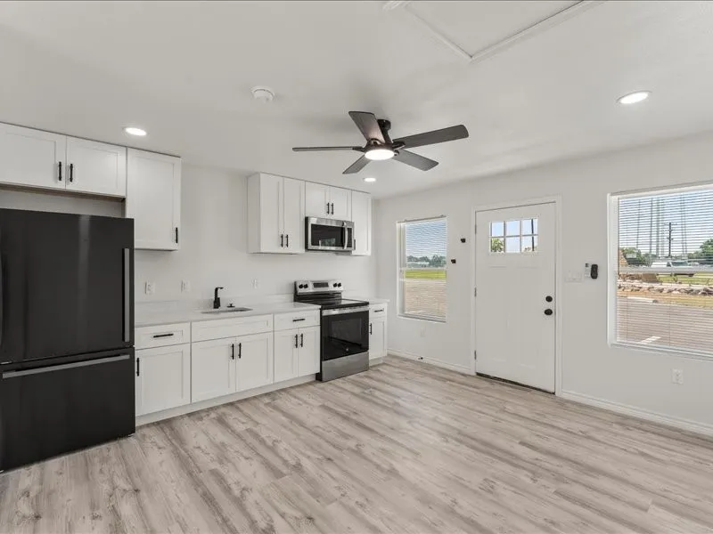 Studio Suites include Kitchenette featuring white cabinetry, wood-finish flooring, a stainless steel microwave, and a black refrigerator