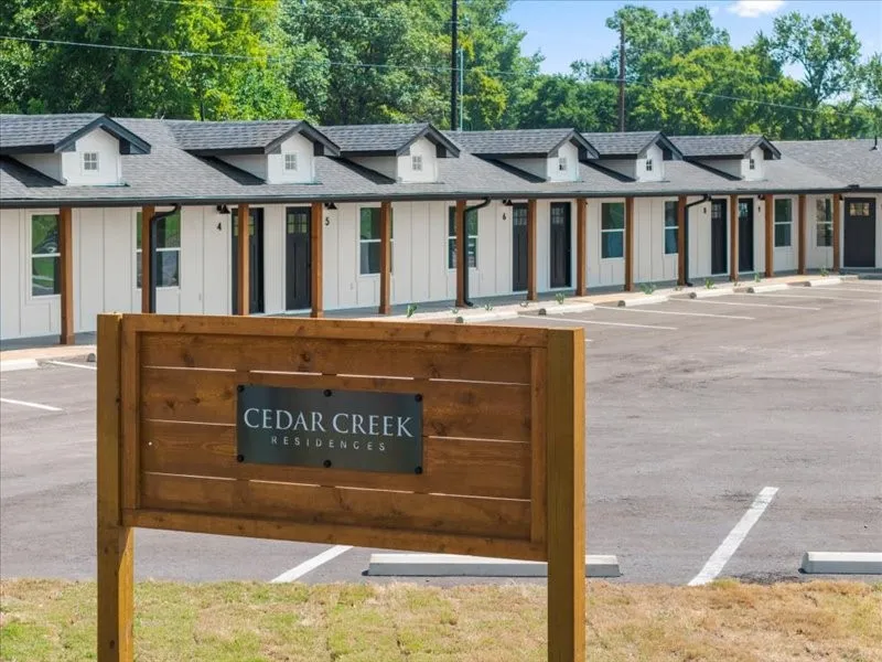 Cedar Creek Residences signage, white vertical siding, dark roof, multiple dormer windows, and covered entrances