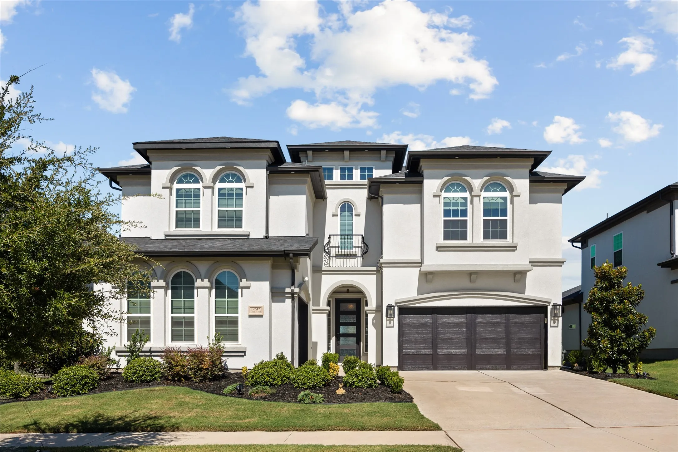 Stucco exterior with arched windows, dark-frame garage doors, and a decorative balcony