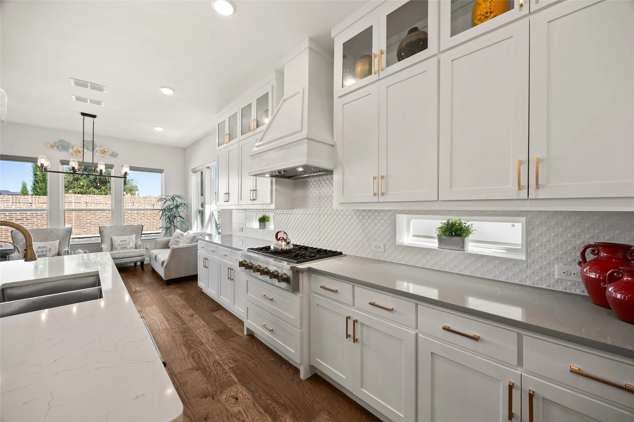 White shaker cabinetry with gold-tone hardware, wood-finish flooring, white diamond-patterned backsplash, and integrated stainless steel appliances