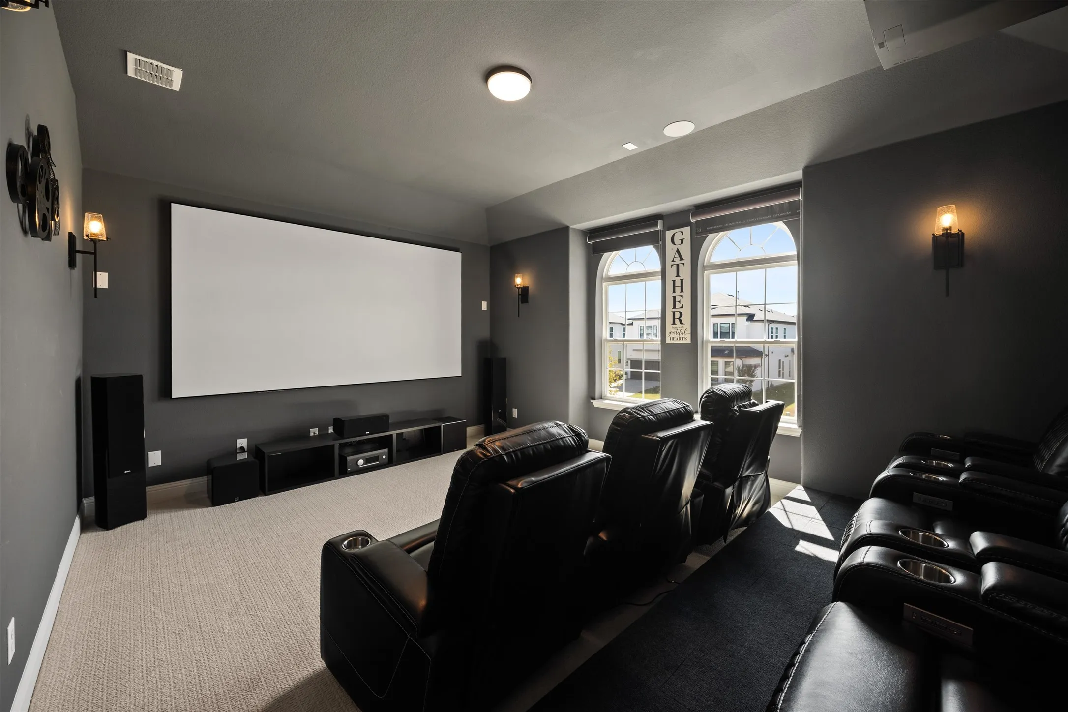 Dedicated media room featuring a large projection screen, recessed lighting, wall-mounted sconces, and arched windows