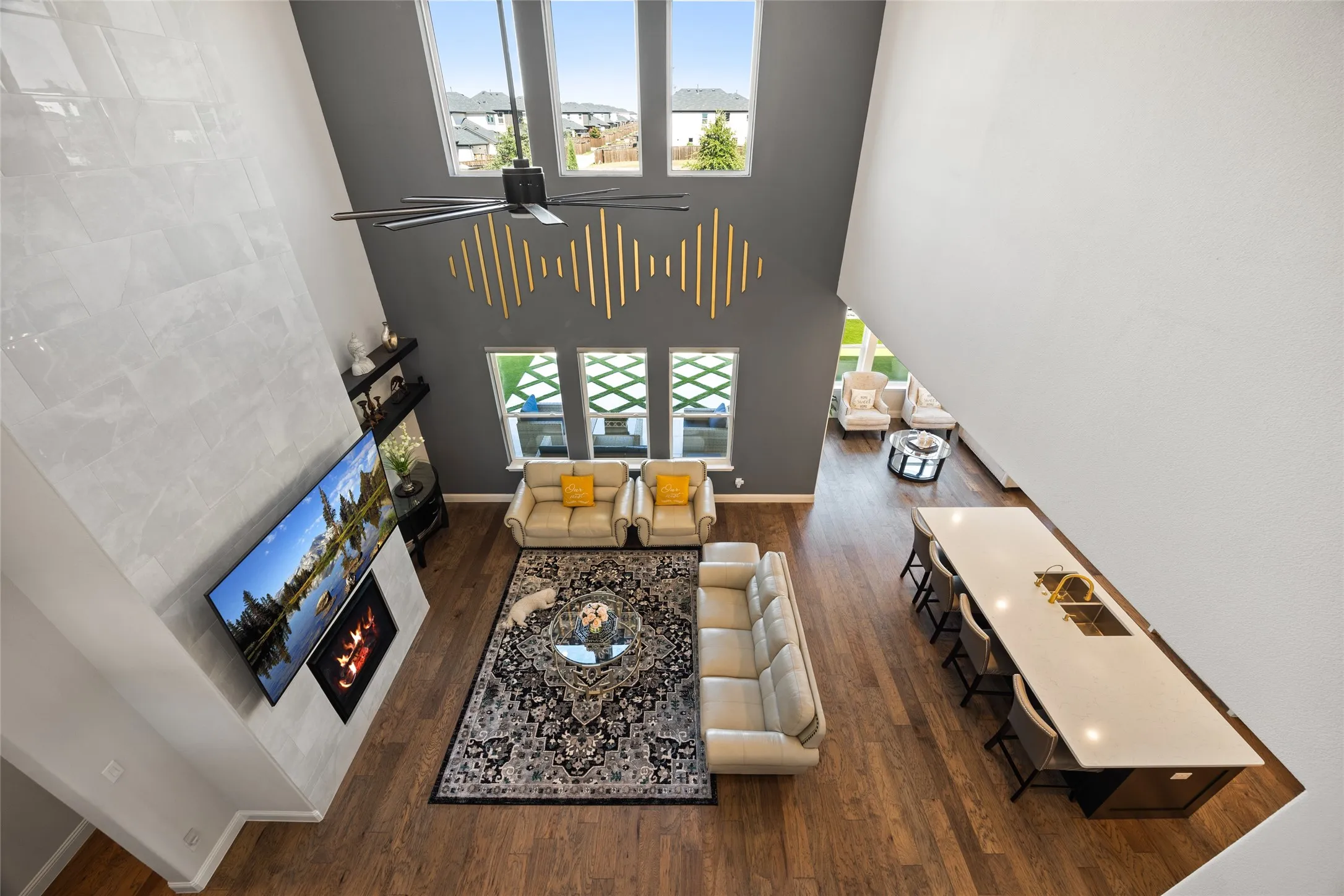 Double-height great room featuring a tall tiled fireplace surround, high ceilings, wood-finish flooring, and an expansive kitchen island with seating