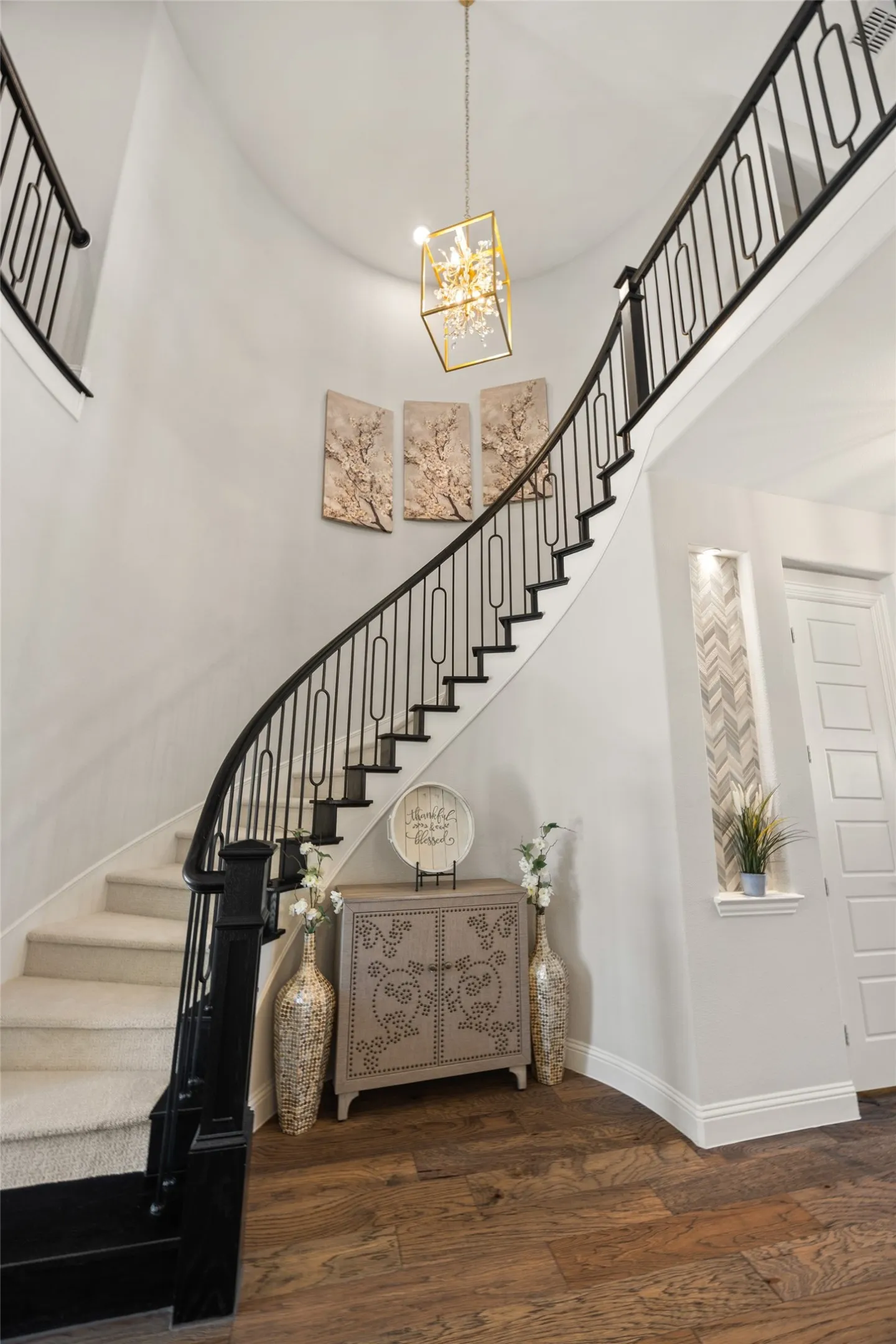 Curved staircase with black metal balusters, carpeted treads, and a wood newel post