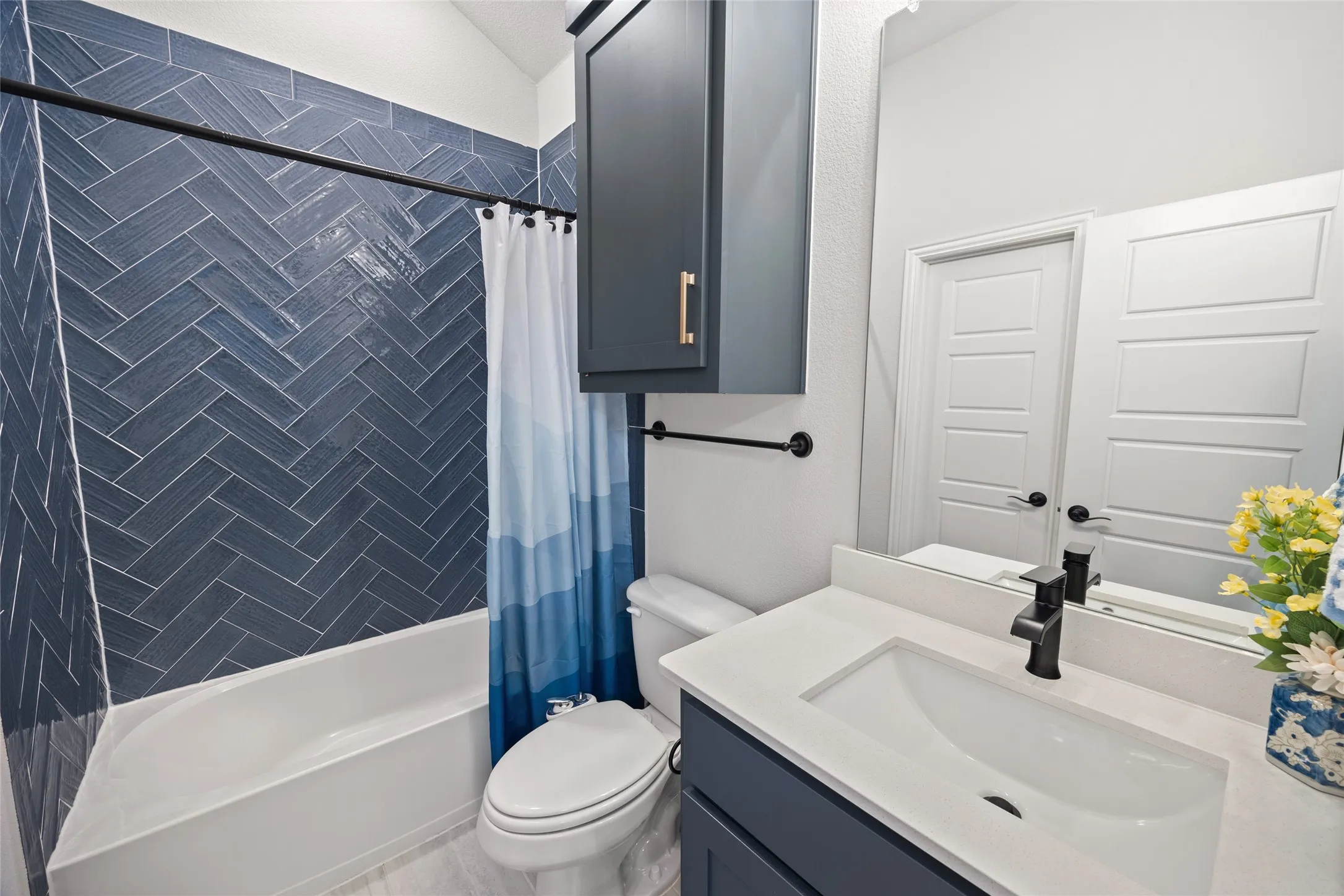 Bathroom featuring a built-in tub with a blue herringbone tile surround, dark blue cabinetry, a white countertop, and a built-in mirror