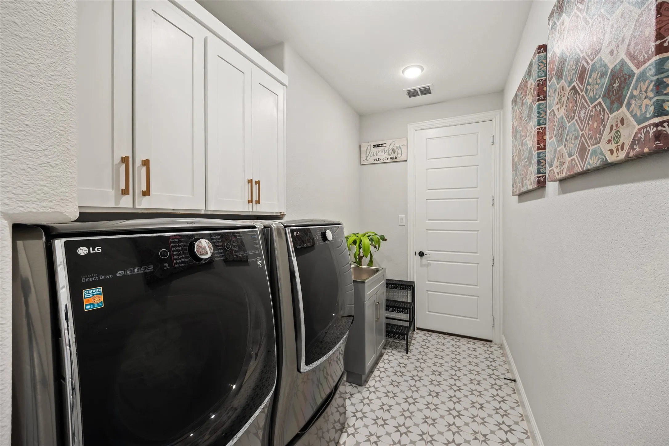 White shaker-style cabinetry with gold-tone hardware, recessed ceiling lighting, five-panel interior door with black hardware, patterned floor tile, and a built-in utility sink