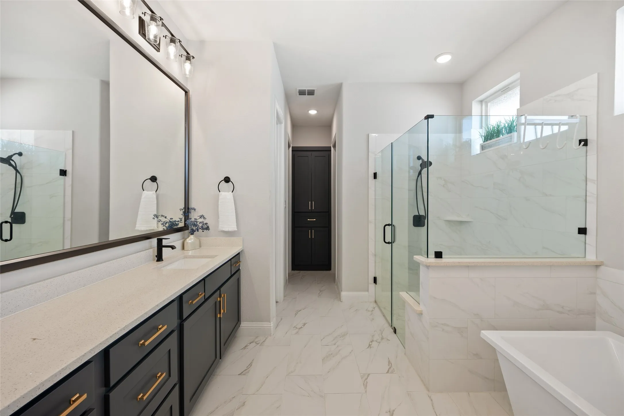 Spacious bathroom featuring a double vanity with ample counter space, a large framed mirror, a separate glass-enclosed shower, a built-in bathtub, and floor-to-ceiling cabinetry