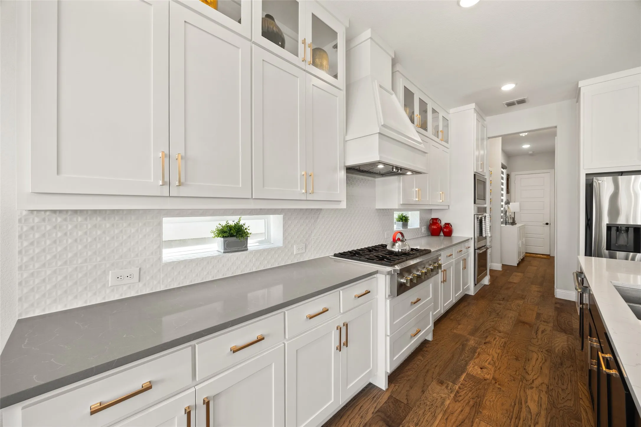 White shaker cabinetry with gold-tone hardware, wood-finish flooring, built-in stainless steel oven, and a gas range