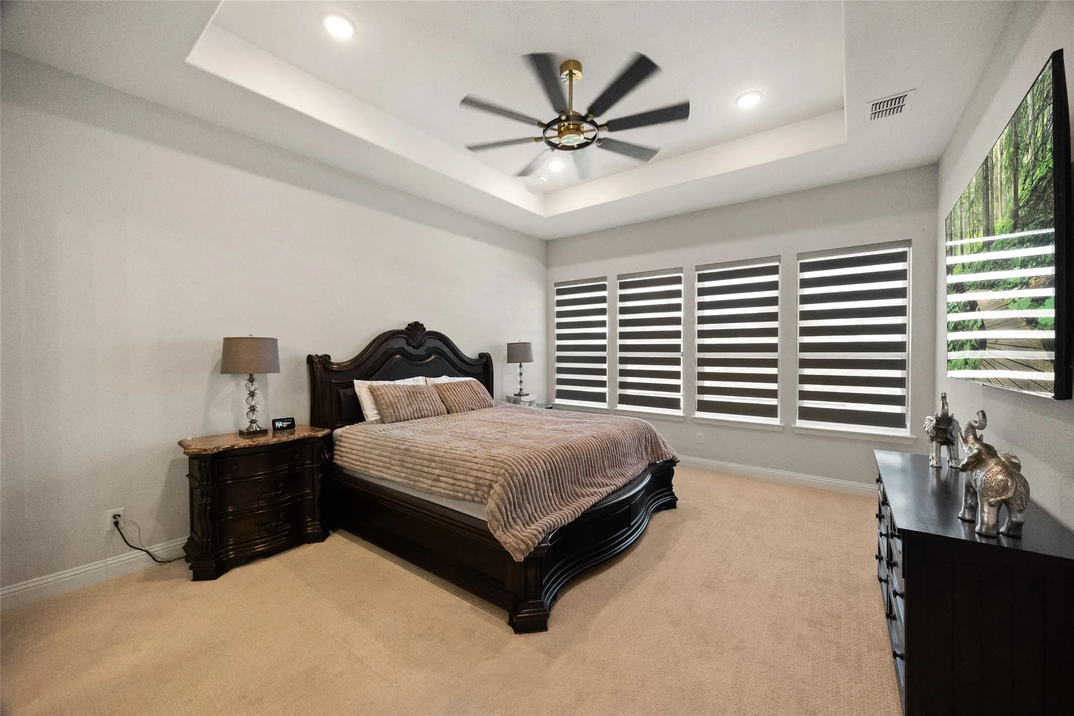 Recessed lighting, tray ceiling, ceiling fan, carpet flooring, and multiple windows with blinds