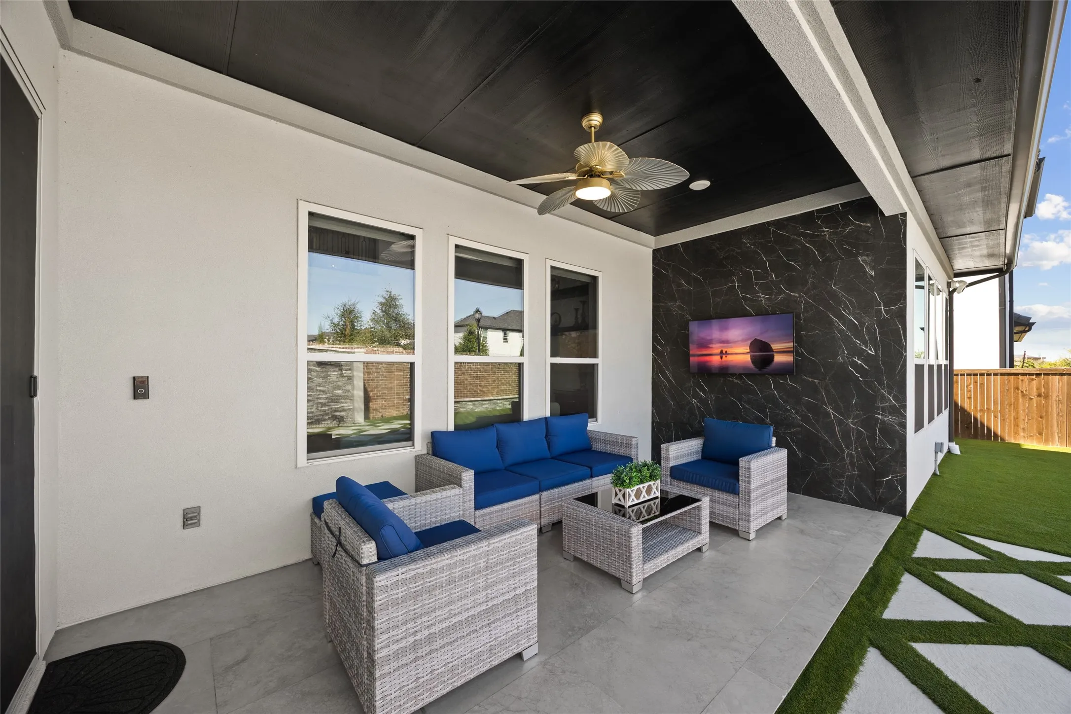 Covered patio featuring a black ceiling with a ceiling fan, a black marble-effect accent wall, and a concrete paver floor