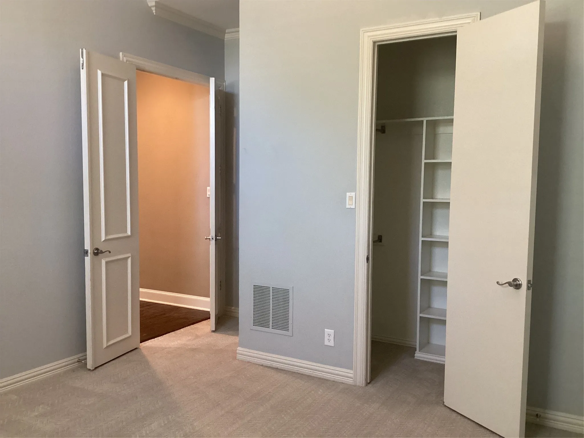 Plush carpet flooring, crown molding, paneled interior door, built-in shelving, and brushed nickel hardware