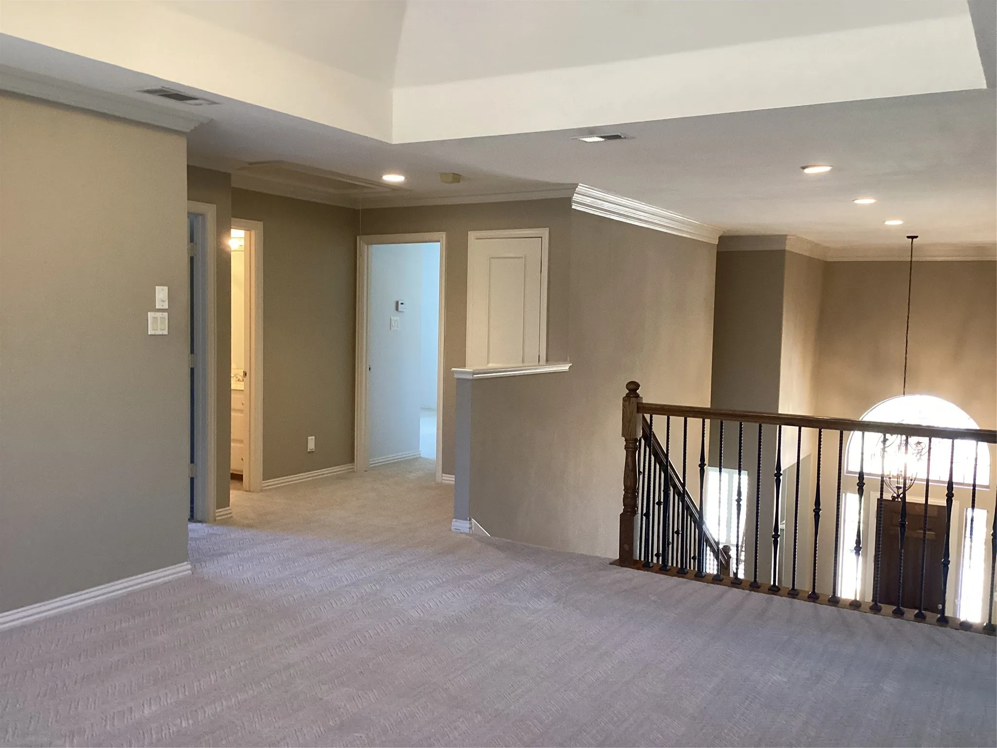 Carpeted upper level featuring a vaulted ceiling with recessed lighting, crown molding, and an open stairwell with wrought iron balusters