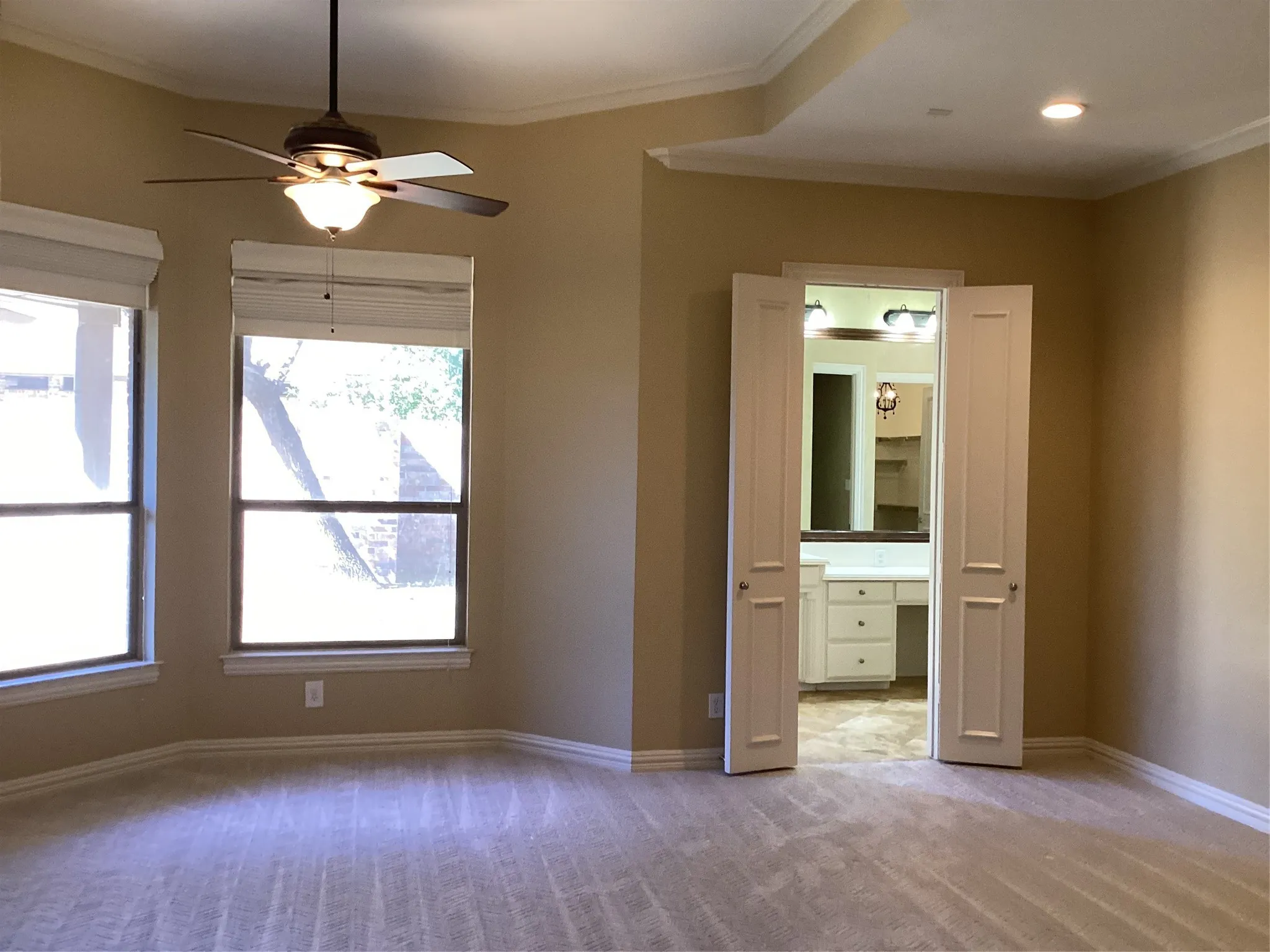 Bay windows with blinds, ceiling fan with integrated lighting, recessed lighting, double doors opening to an adjoining space, and crown molding