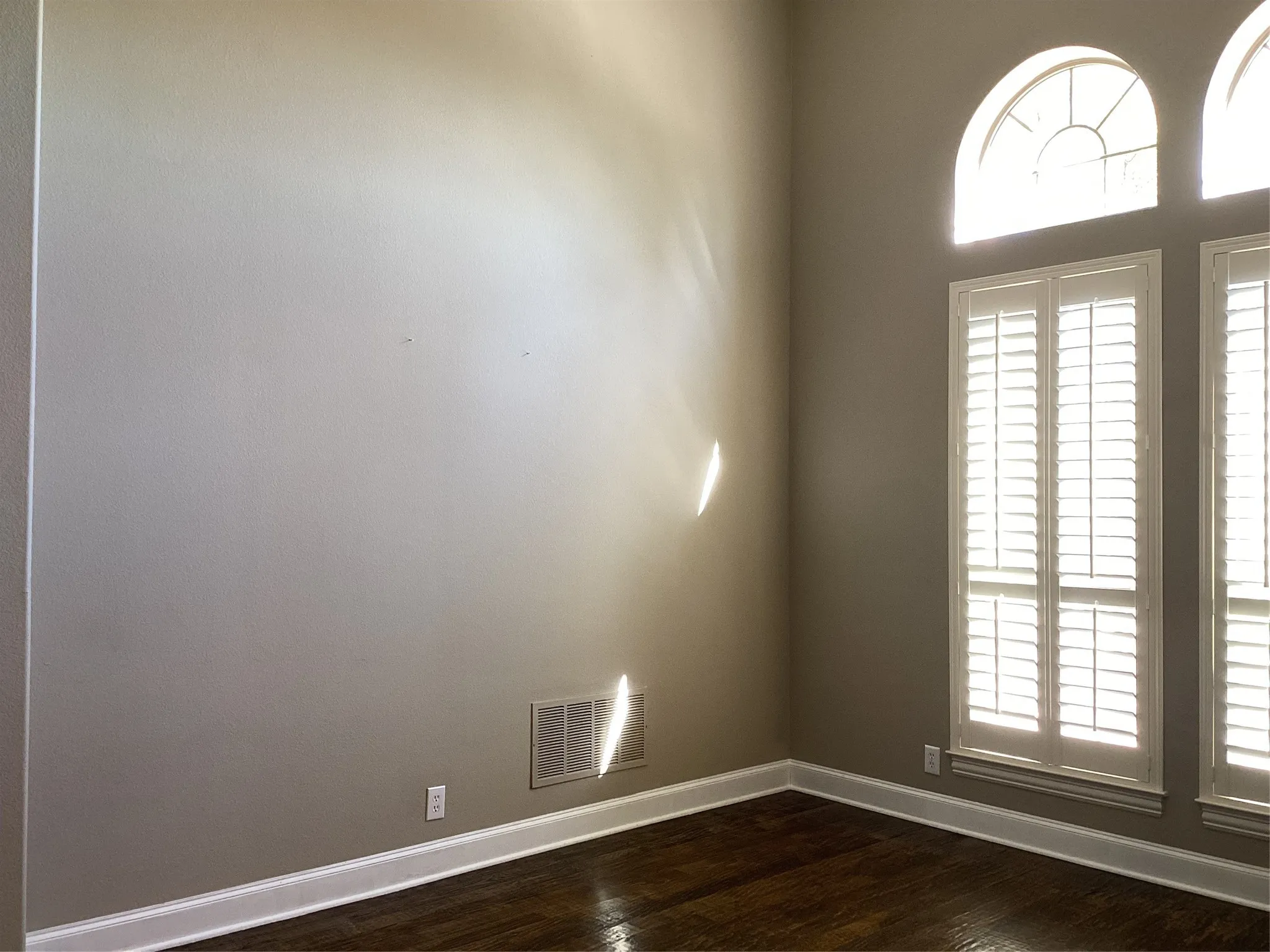 Arched transom windows, plantation shutters, wood-finish flooring, and white trim