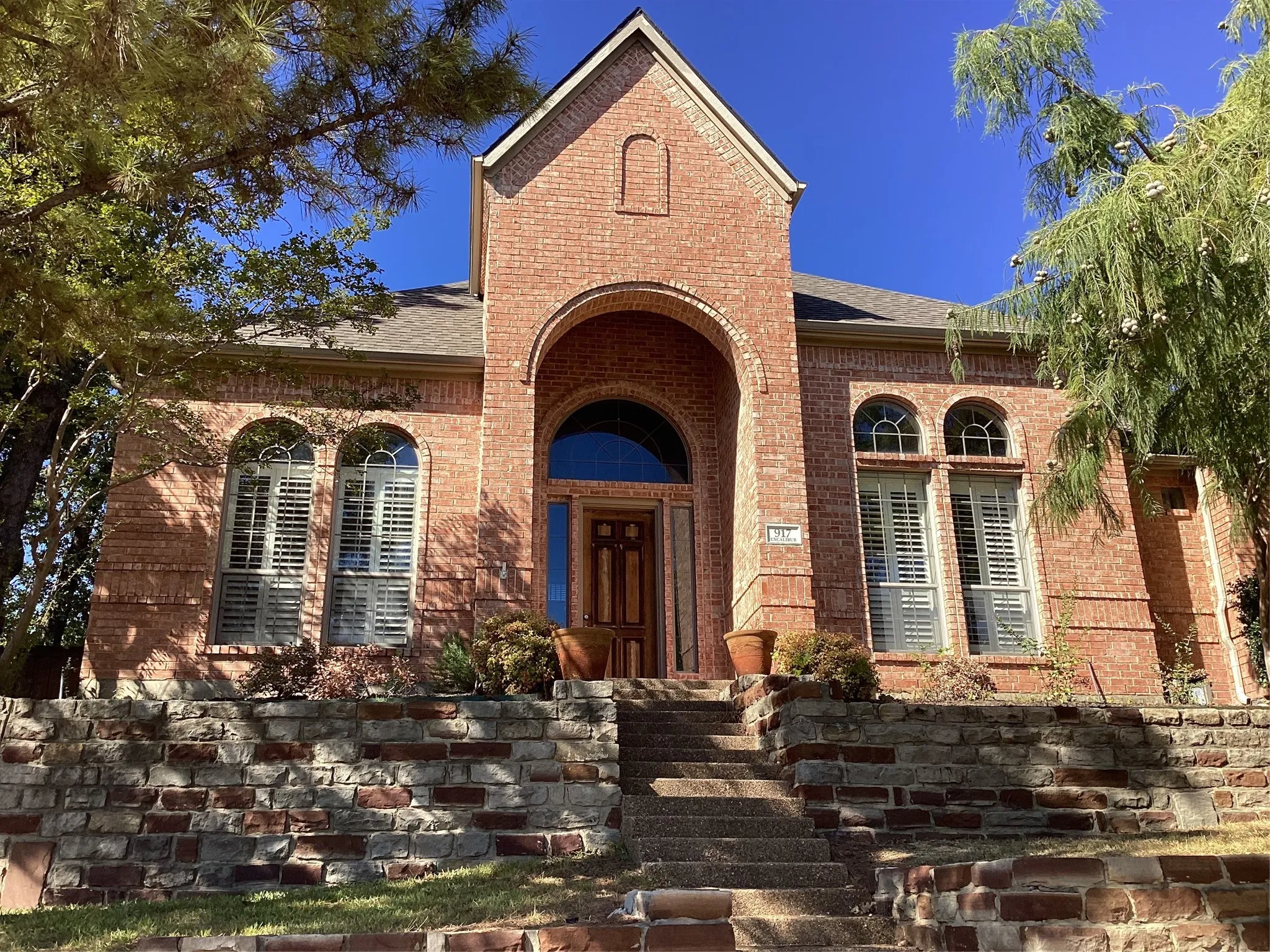 Brick exterior with arched entryway, multi-paned arched windows, and stone-clad retaining walls