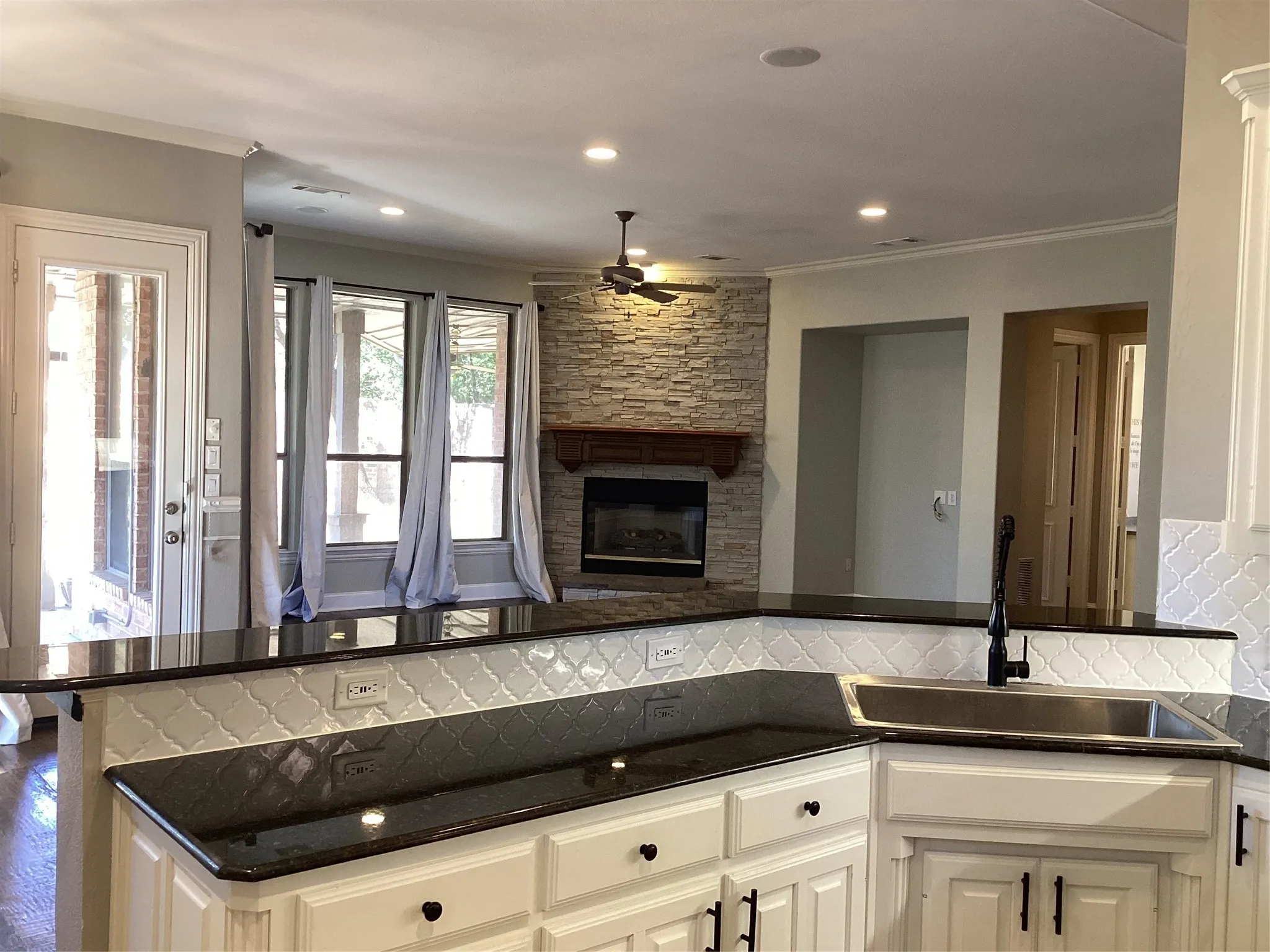 Kitchen with dark countertops, white cabinetry, integrated sink, and an arabesque tile backsplash