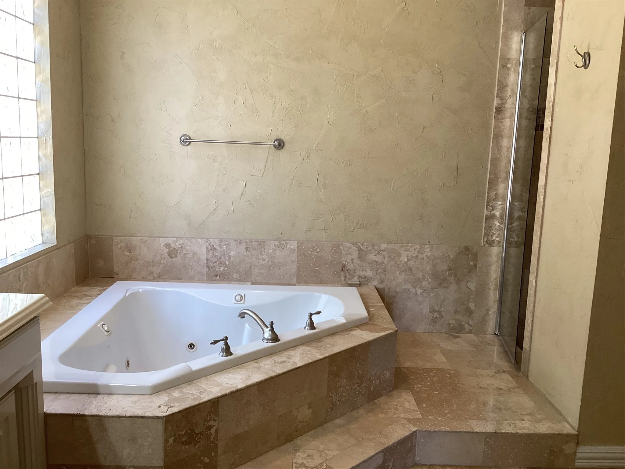Corner soaking tub with dual-tone fixtures, surrounded by natural stone tiling and a textured wall finish
