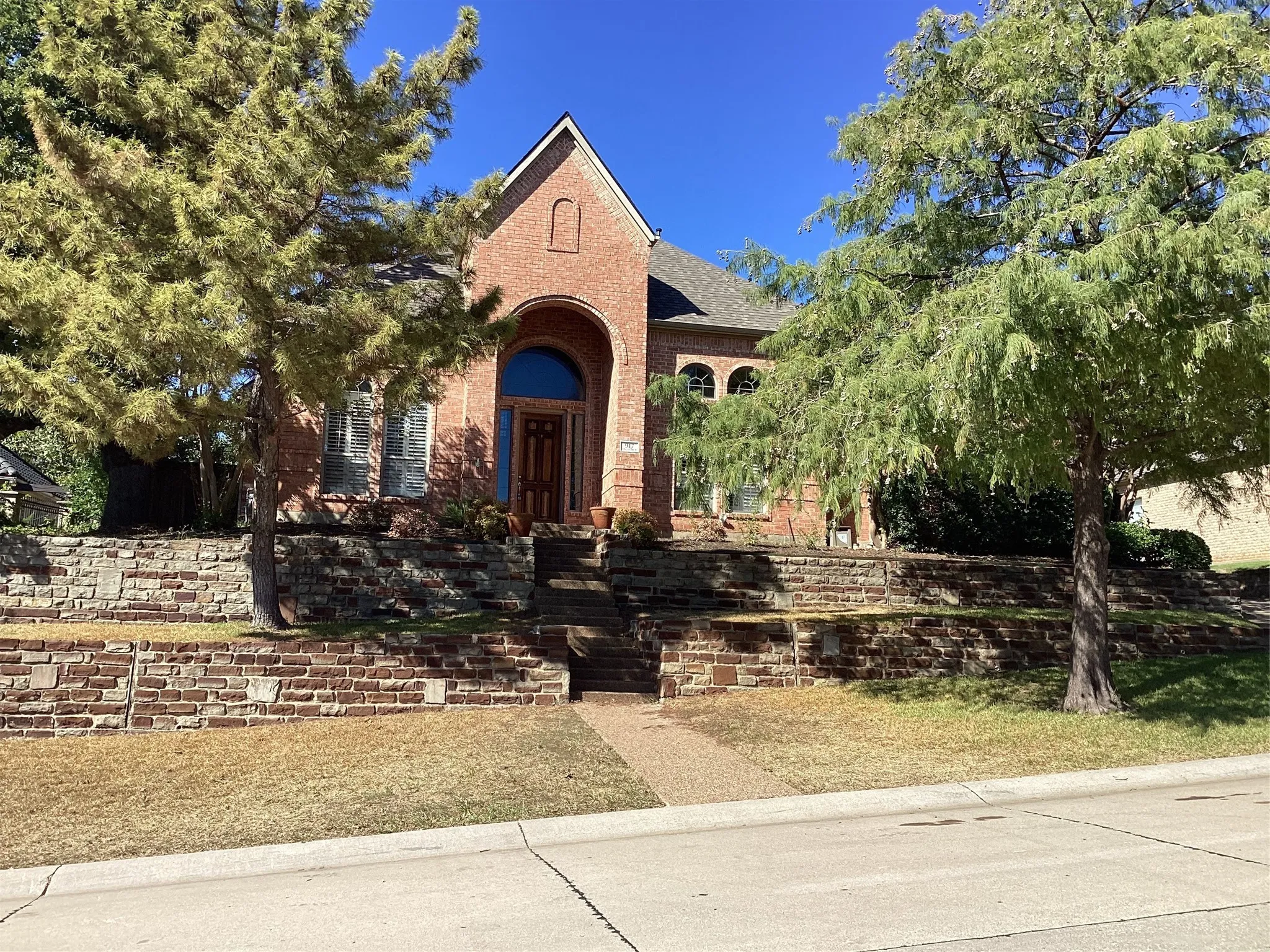 Red brick exterior with an arched entryway, multiple arched windows, and a multi-tiered stone retaining wall