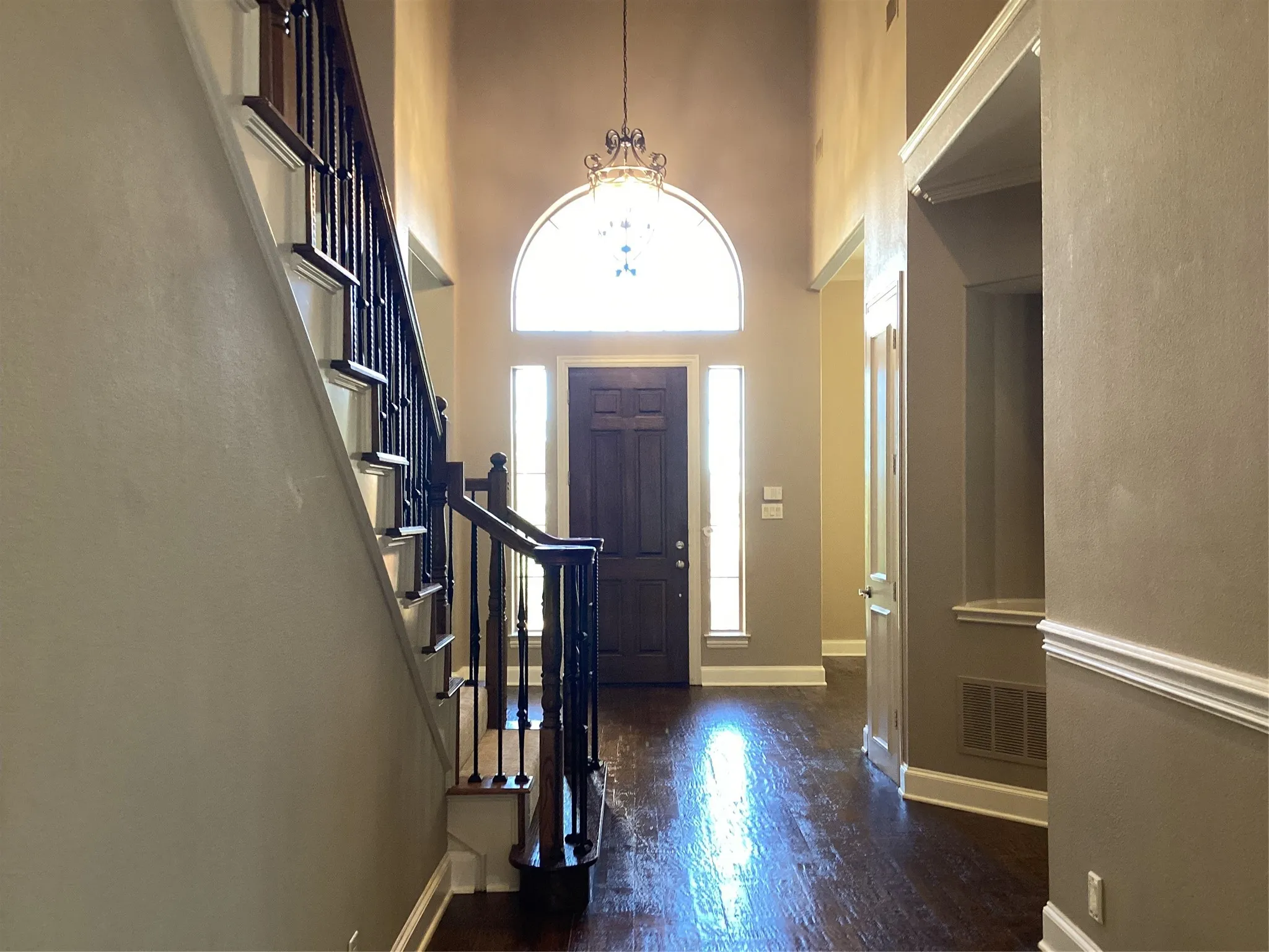 Two-story entry with wood-finish flooring, staircase with wrought iron balusters, transom window, sidelight windows, and decorative chandelier