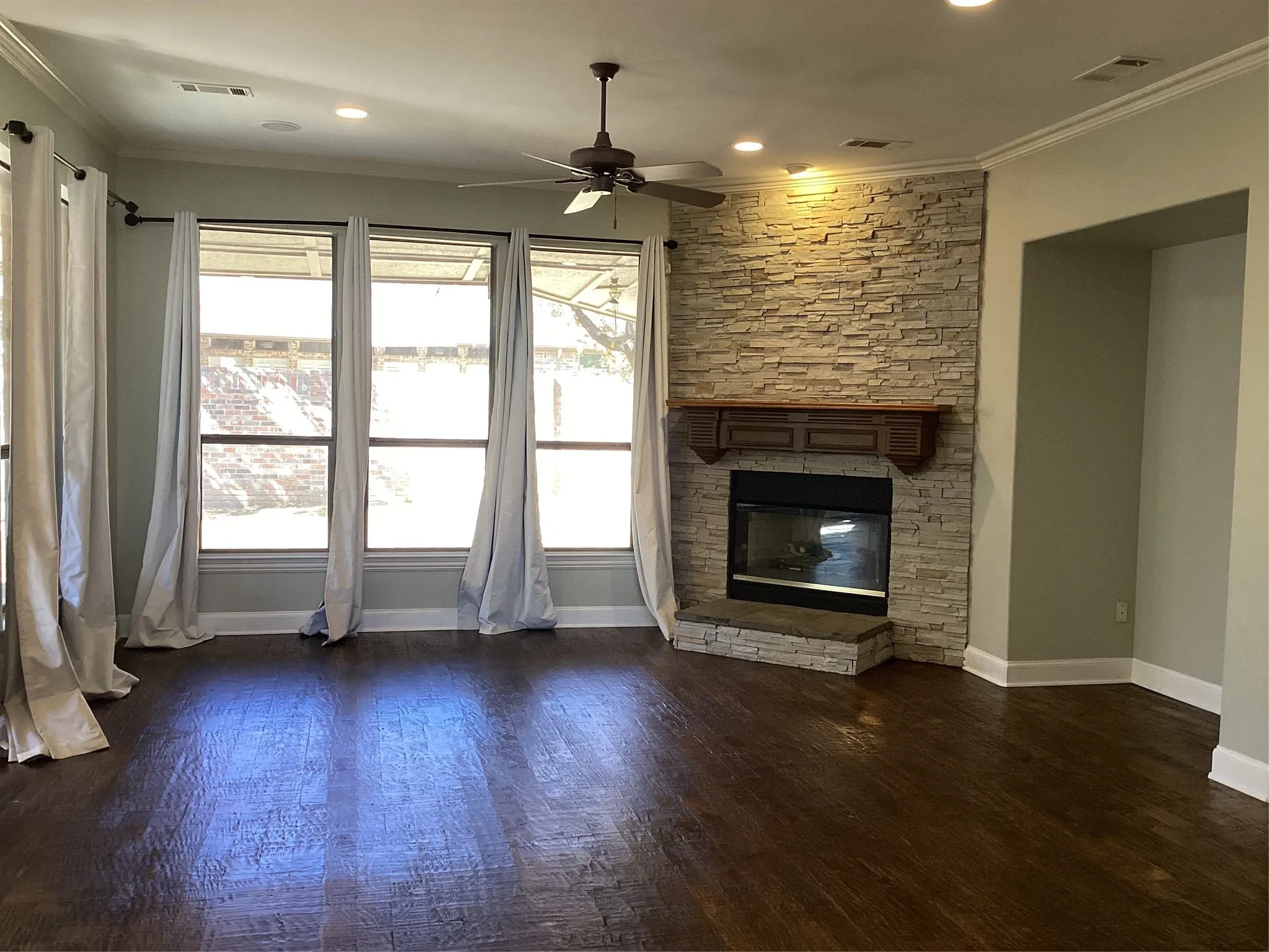 Living area with wood-finish flooring, a stacked stone fireplace with a wood mantle, and multiple windows
