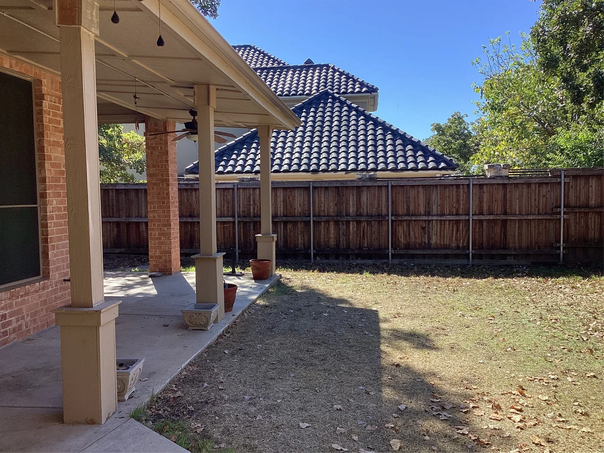 Covered patio with a concrete slab, brick exterior, and a wood-slat privacy fence