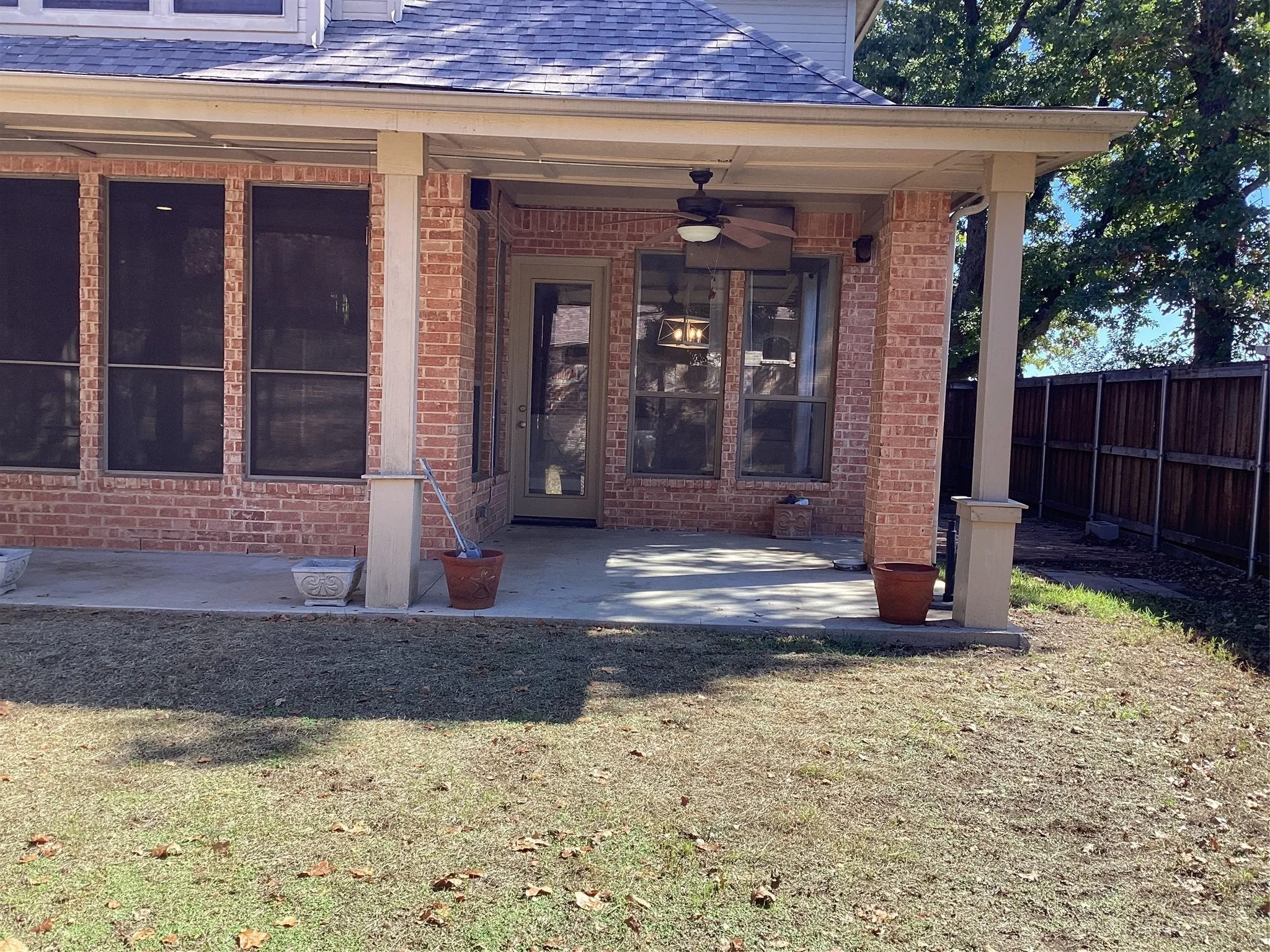 Covered patio featuring brick columns, a ceiling fan, and a wood privacy fence