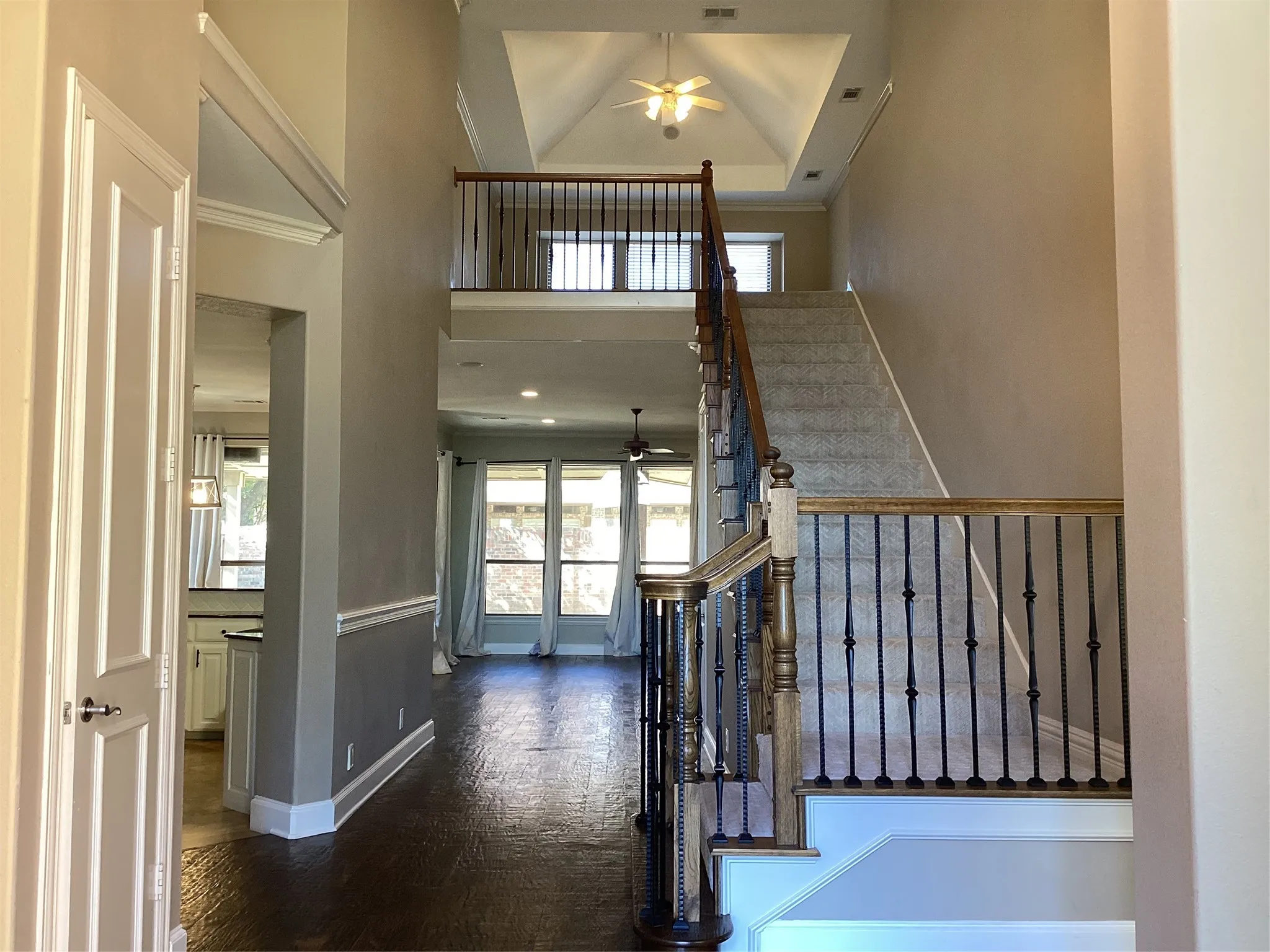 Two-story foyer with wood-finish flooring, a carpeted staircase featuring wrought iron balusters and wood handrails, and a tray ceiling