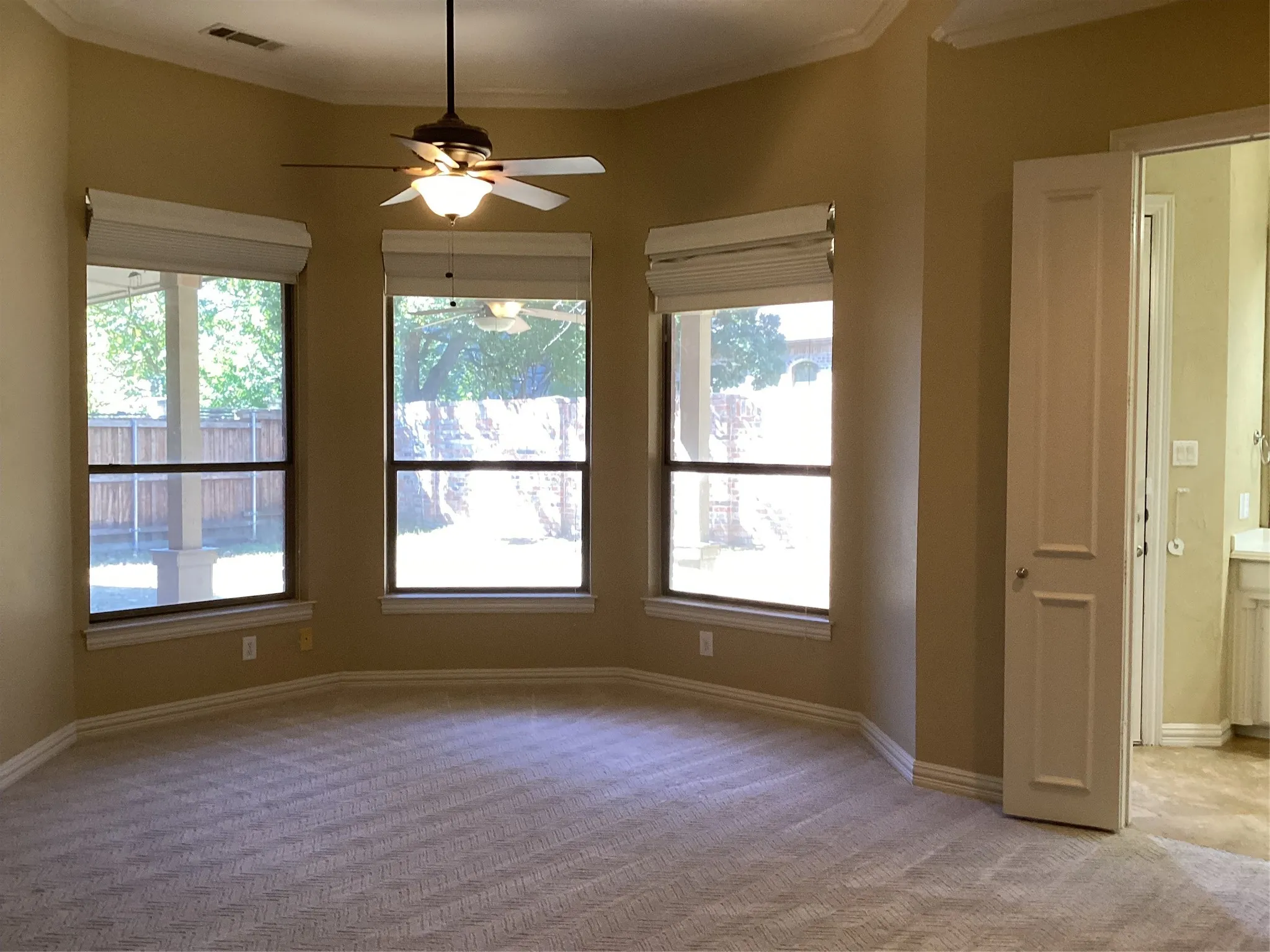 Bay window with three large windows, ceiling fan with integrated lighting, crown molding, and neutral carpeting