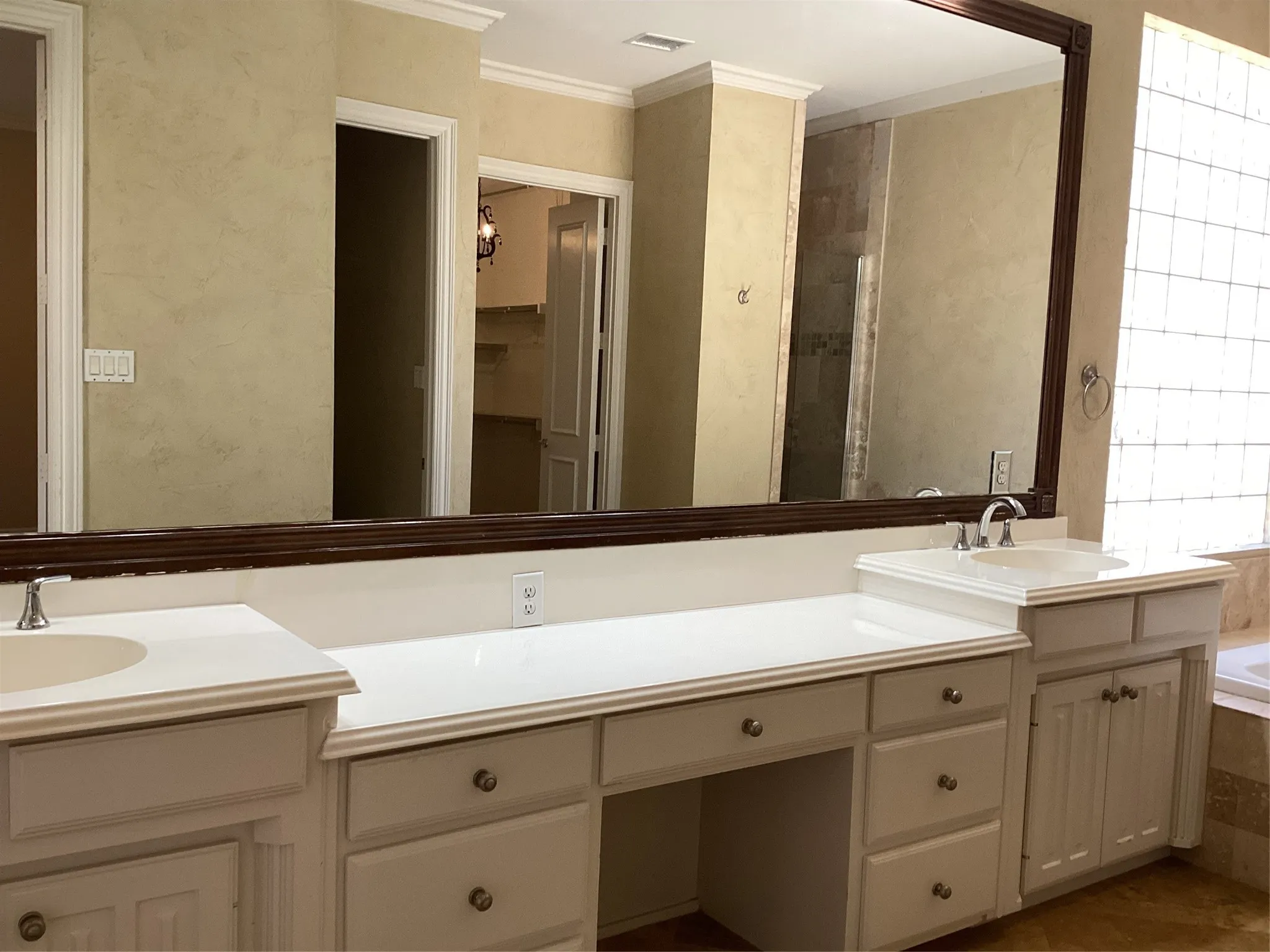 Dual vanity with integrated sinks, white countertops, built-in cabinetry, and large framed mirror