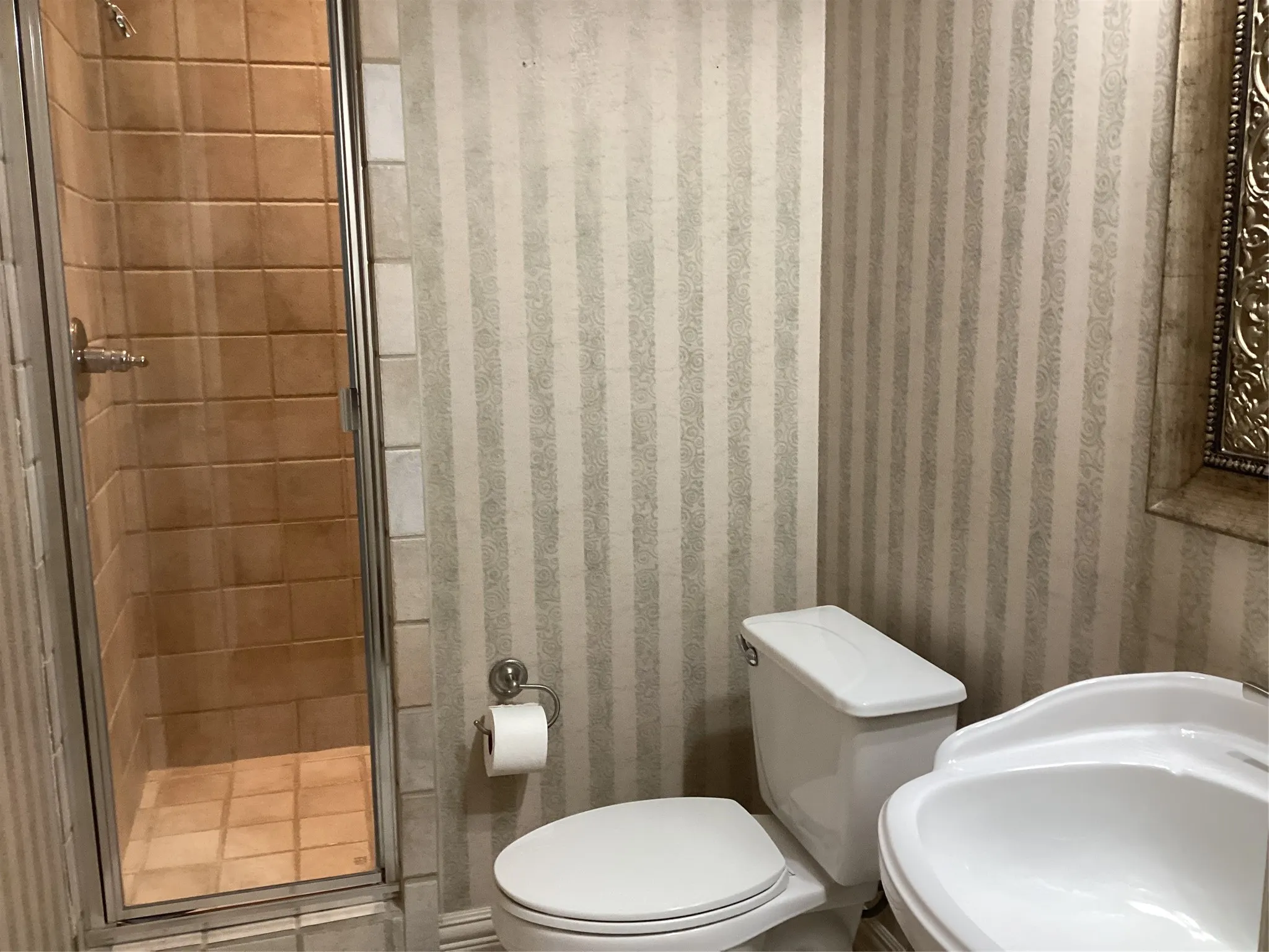 Glass-enclosed shower with square tile surround, pedestal sink, and toilet with a closed-lid tank