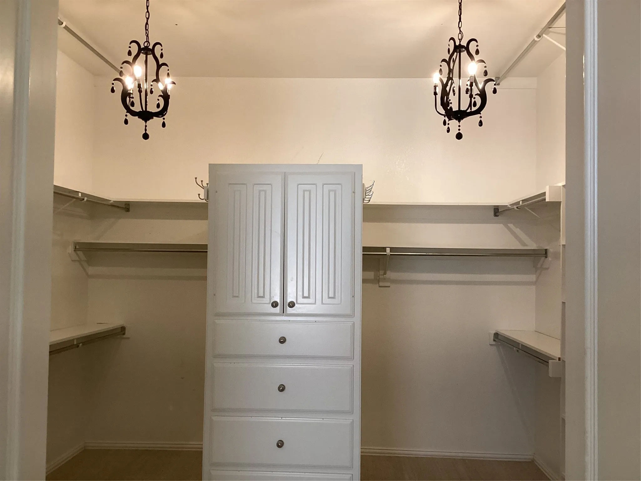 Walk-in closet featuring two ornate chandeliers, built-in cabinetry with paneled doors and drawers, and extensive shelving and hanging rods
