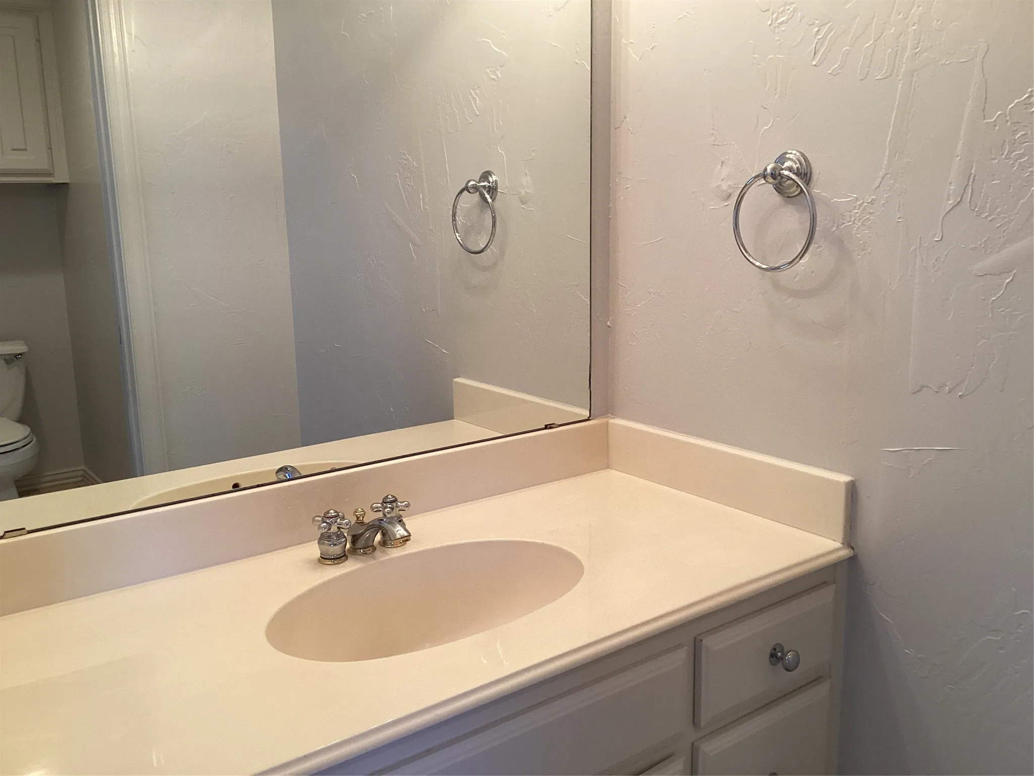Integrated vanity with an oval sink, polished chrome faucet, and white cabinetry with round silver-toned pulls