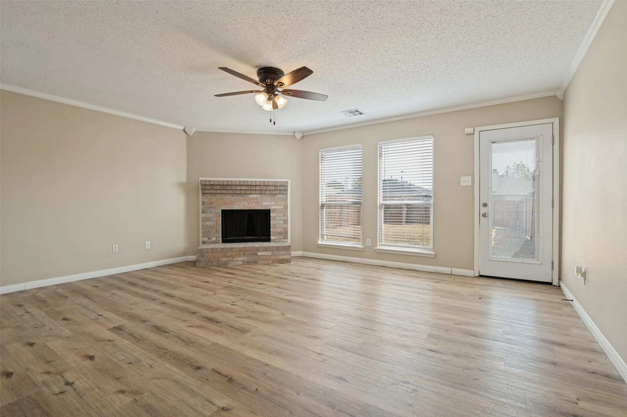 Living area featuring wood-finish flooring, a brick-surround fireplace, a ceiling fan, and multiple windows with blinds