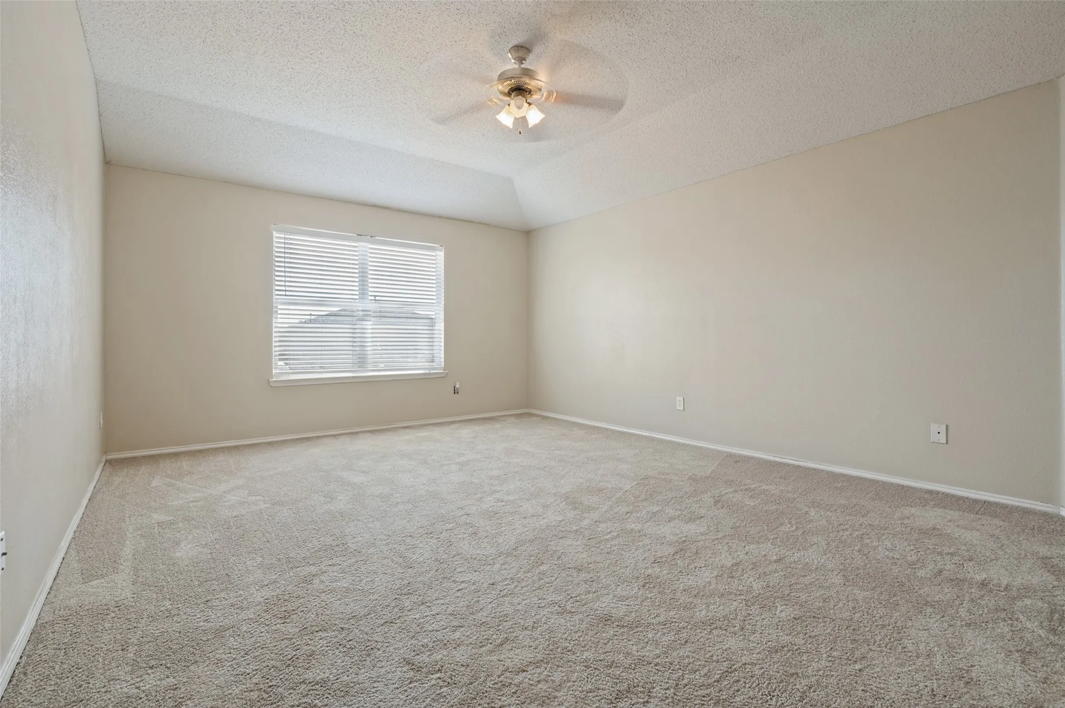 Vaulted ceiling with an attached ceiling fan, large window with horizontal blinds, and carpeting throughout