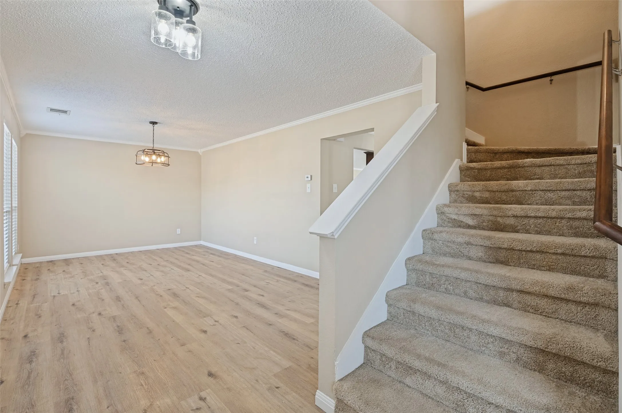 Wood-finish flooring, staircase with carpeted treads, decorative light fixture, crown molding, and a traditional handrail