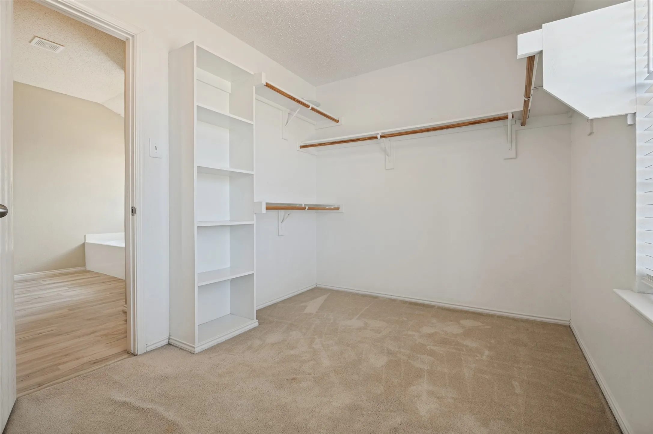 Walk-in closet featuring carpet flooring, built-in shelving, two clothing rods, and a window for natural light