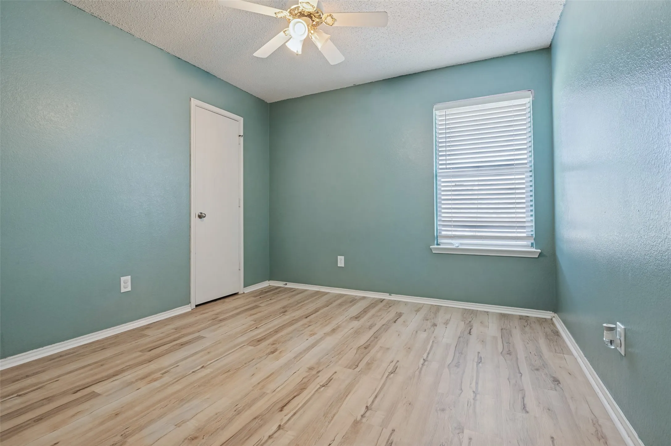 Light wood-finish flooring, ceiling fan with light fixture, and window with horizontal blinds